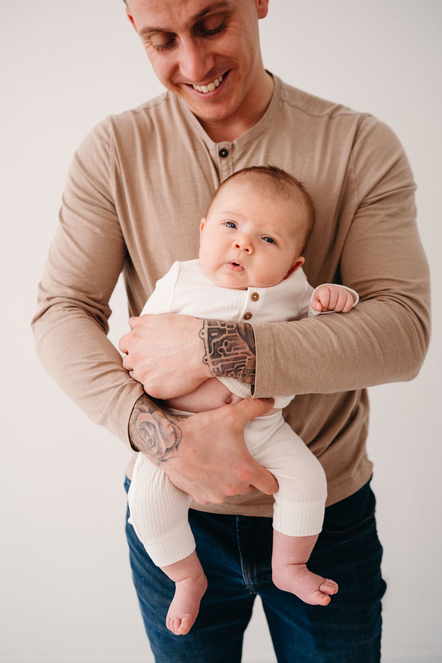 A person in a beige henley shirt holds a baby wearing white clothing.