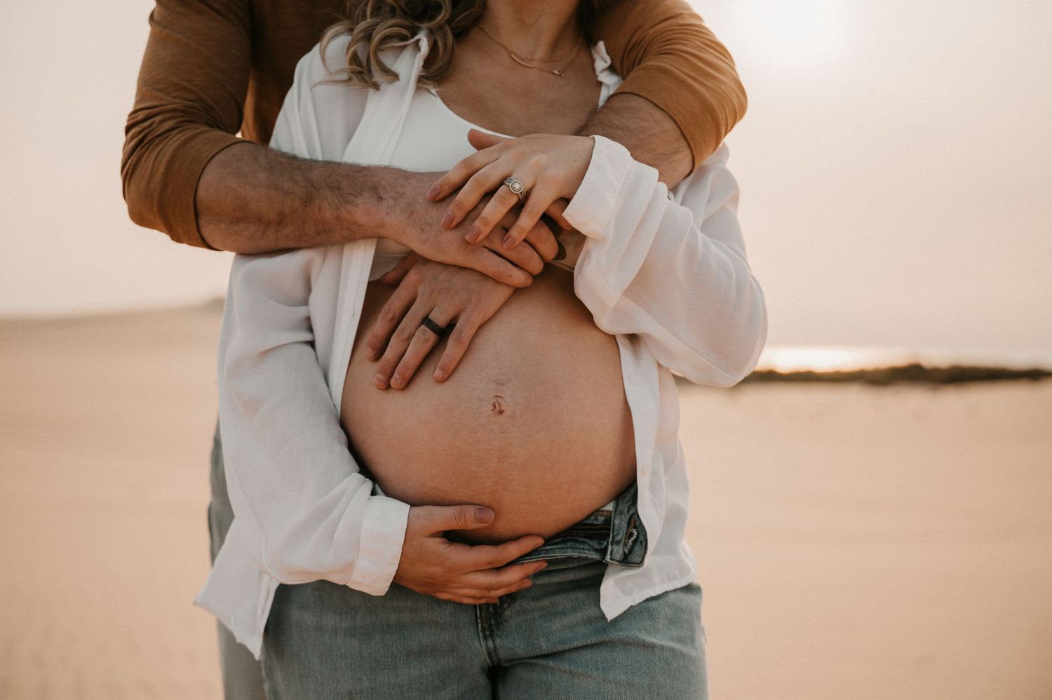 Close-up shot of hands cradling pregnant belly against desert background.