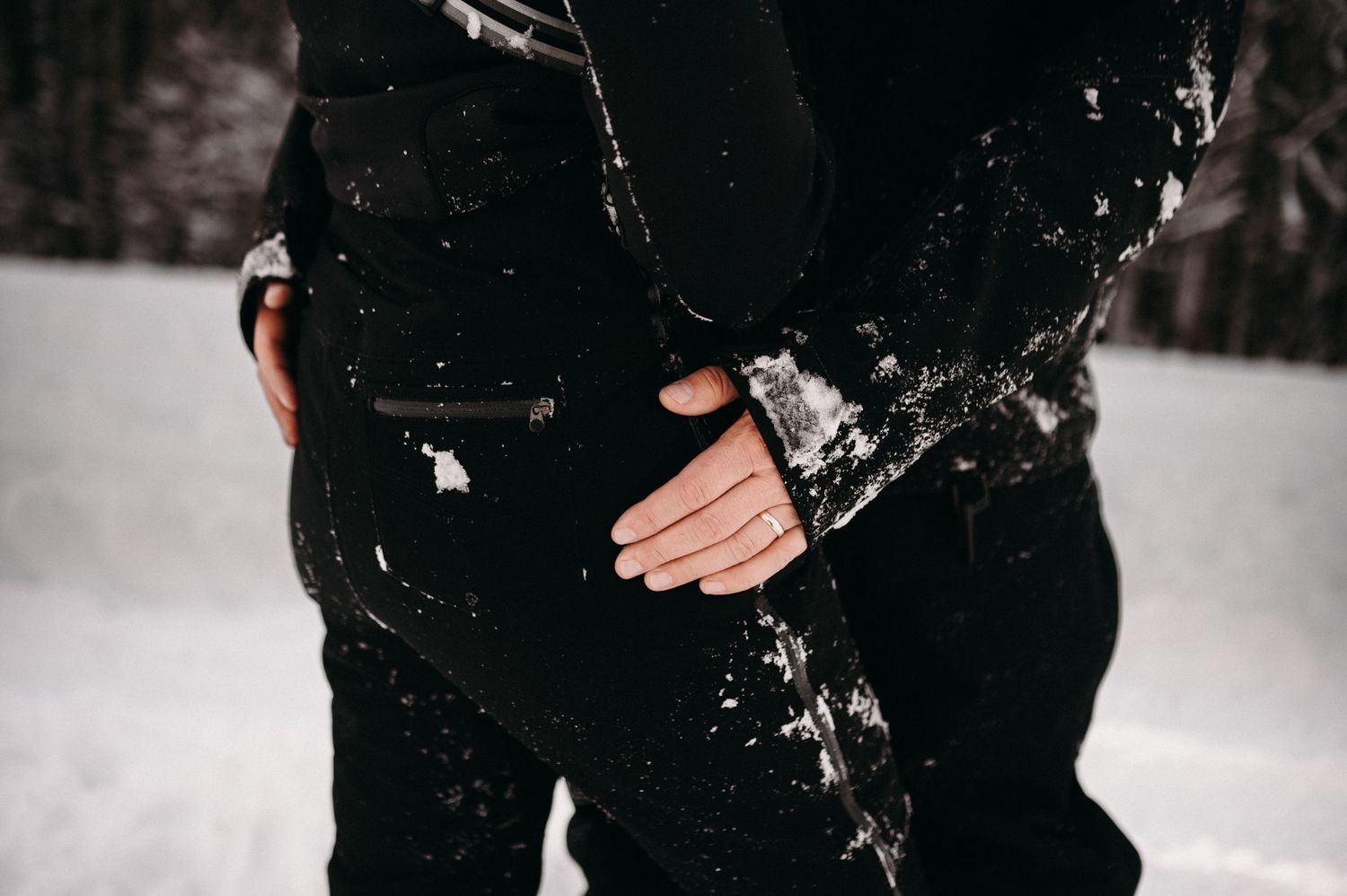 Close-up shot of hands embracing against black snow-covered winter clothing.