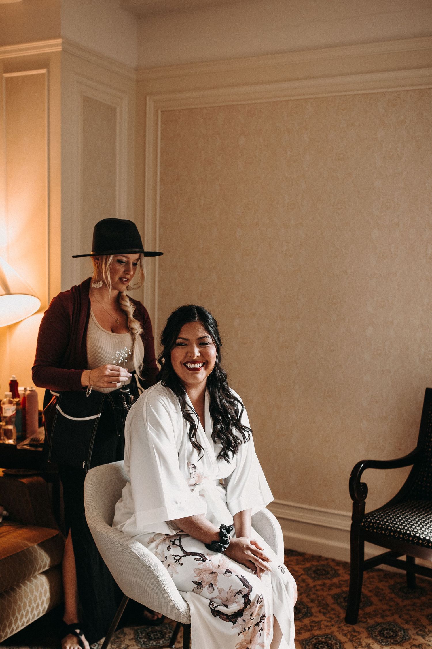Two people share a candid moment in a warmly lit room with elegant decor and a floral robe.