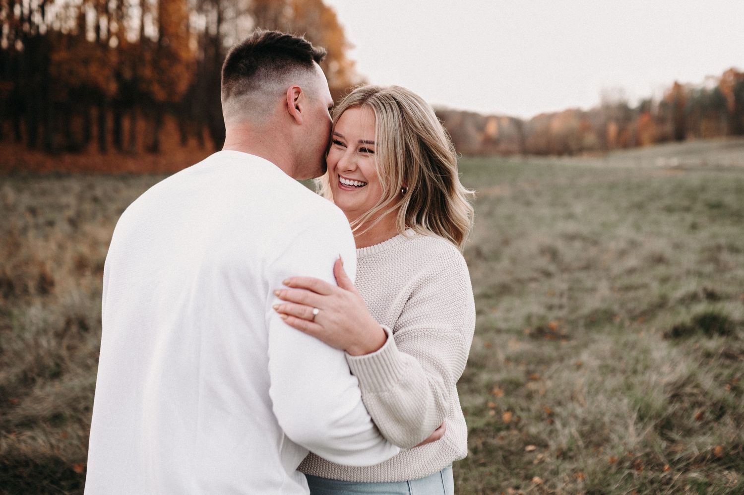 Happy couple sharing tender moment against backdrop of fall trees.