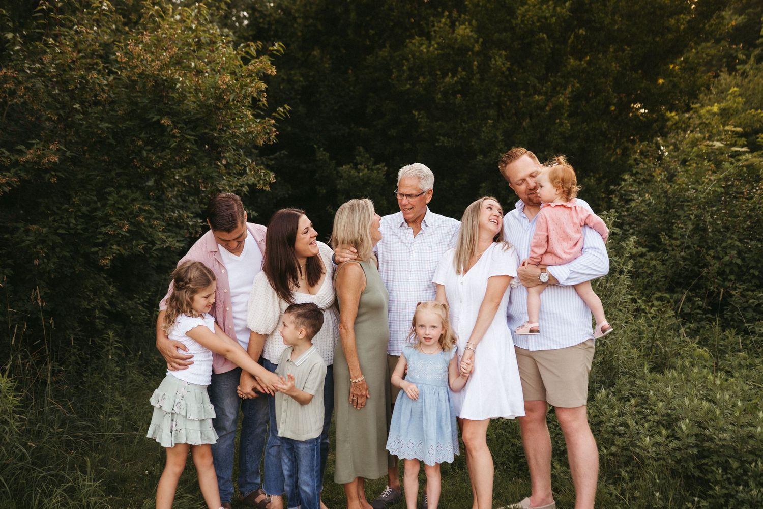 Multi-generational family gathering outdoors for a casual group photo in a natural setting.