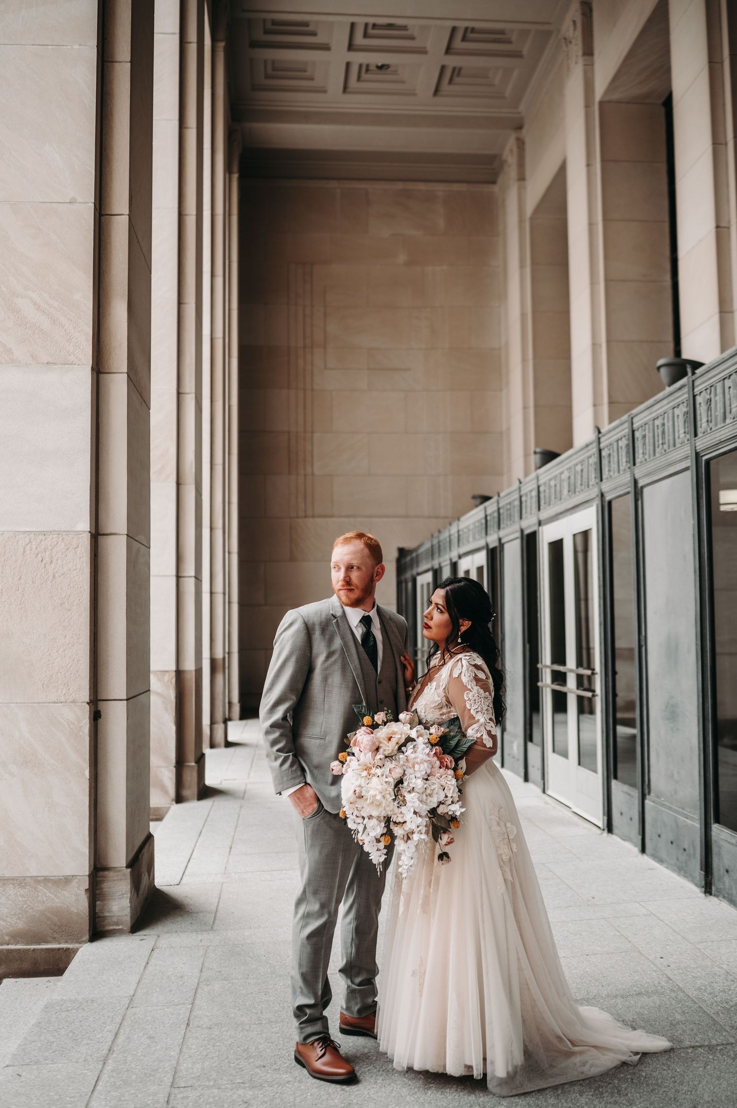 Couple poses together in formal wedding attire against architectural backdrop with columns.