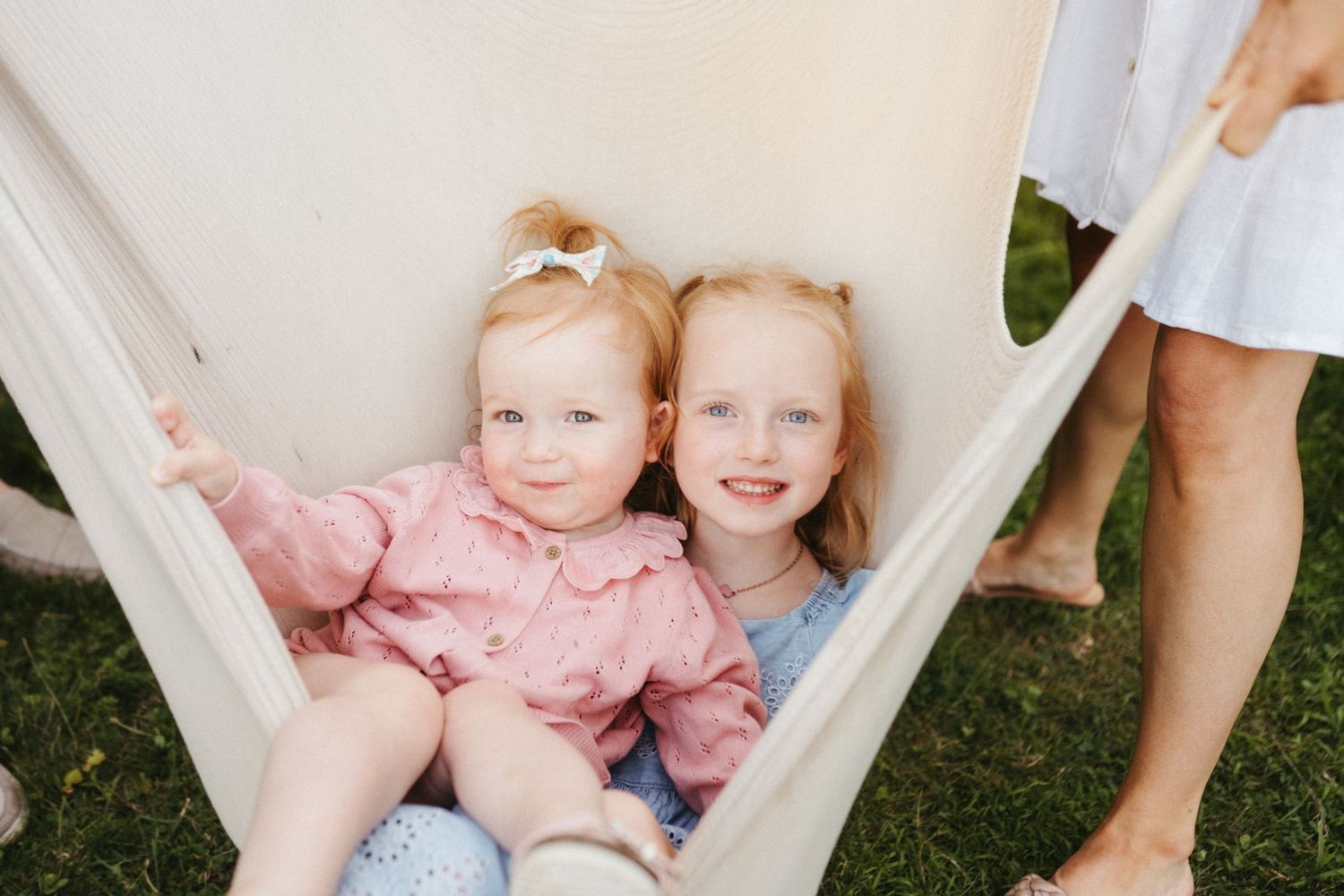 Children playing and being held in a soft white hammock outdoors during a summer photo session.