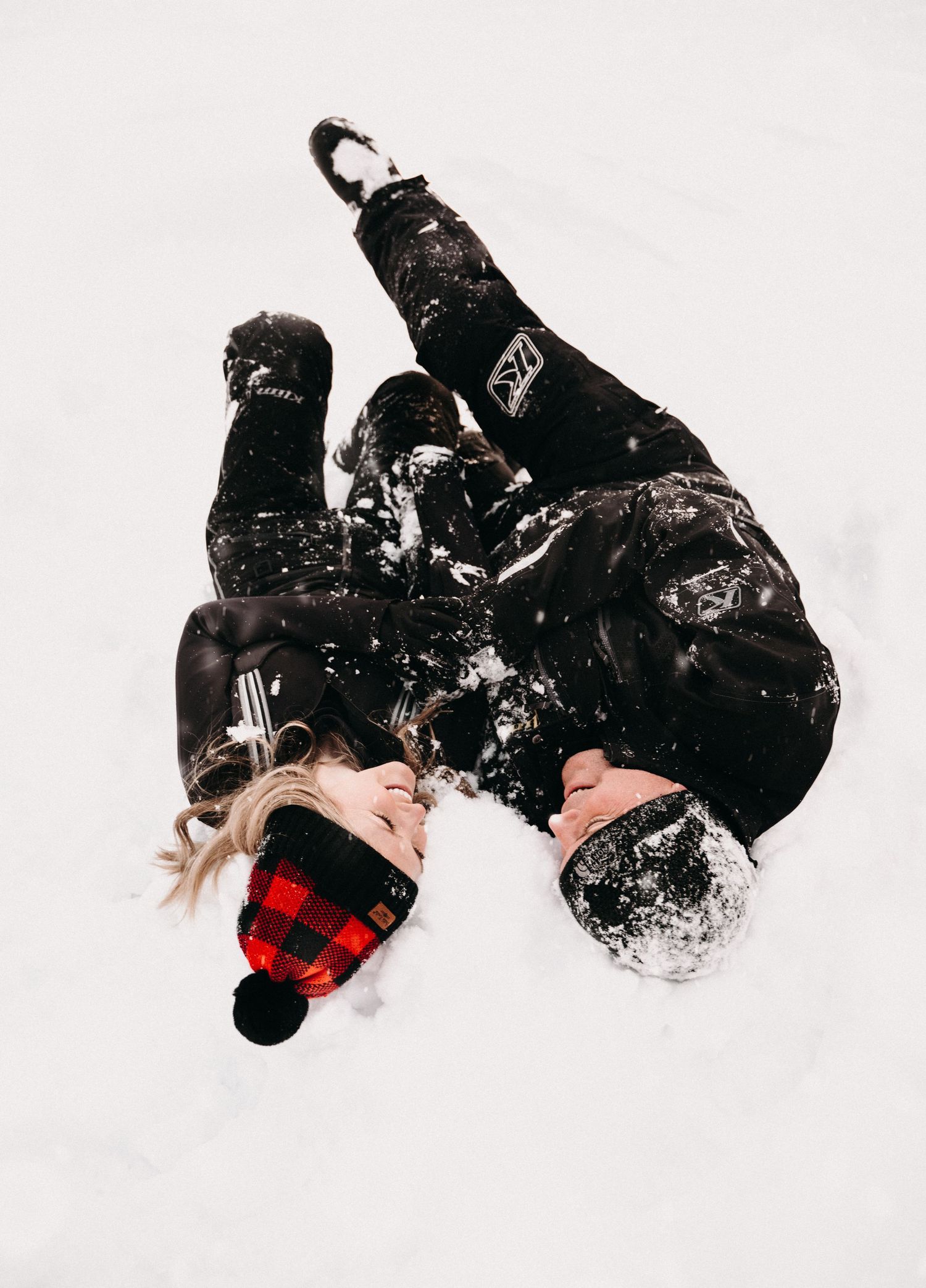 Two people in black winter gear lying in snow captured from above.