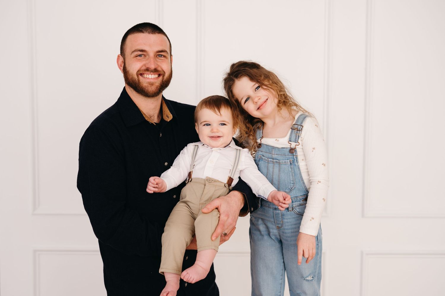 Family group portrait against white wall in casual attire.