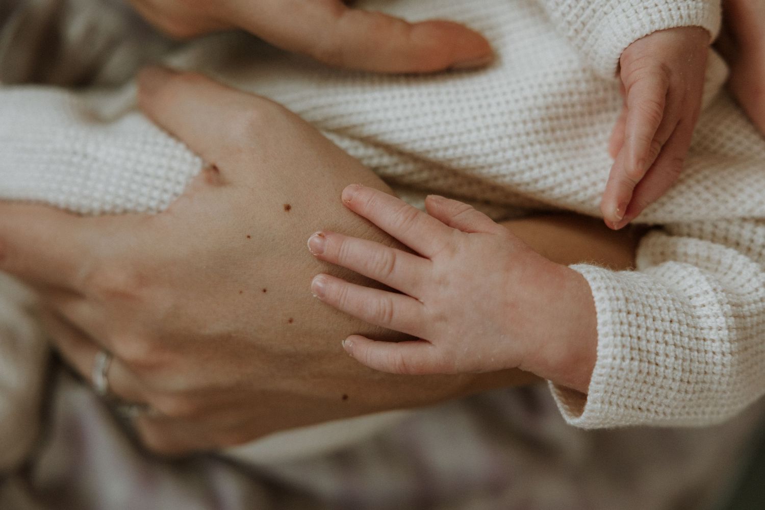 Gentle hands holding and caressing newborn baby in soft white blanket.