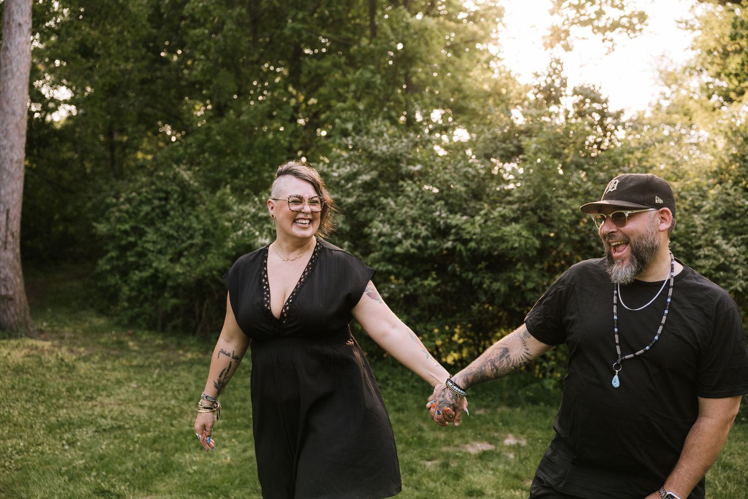 Smiling couple holding hands and walking together through a lush green outdoor setting at sunset.