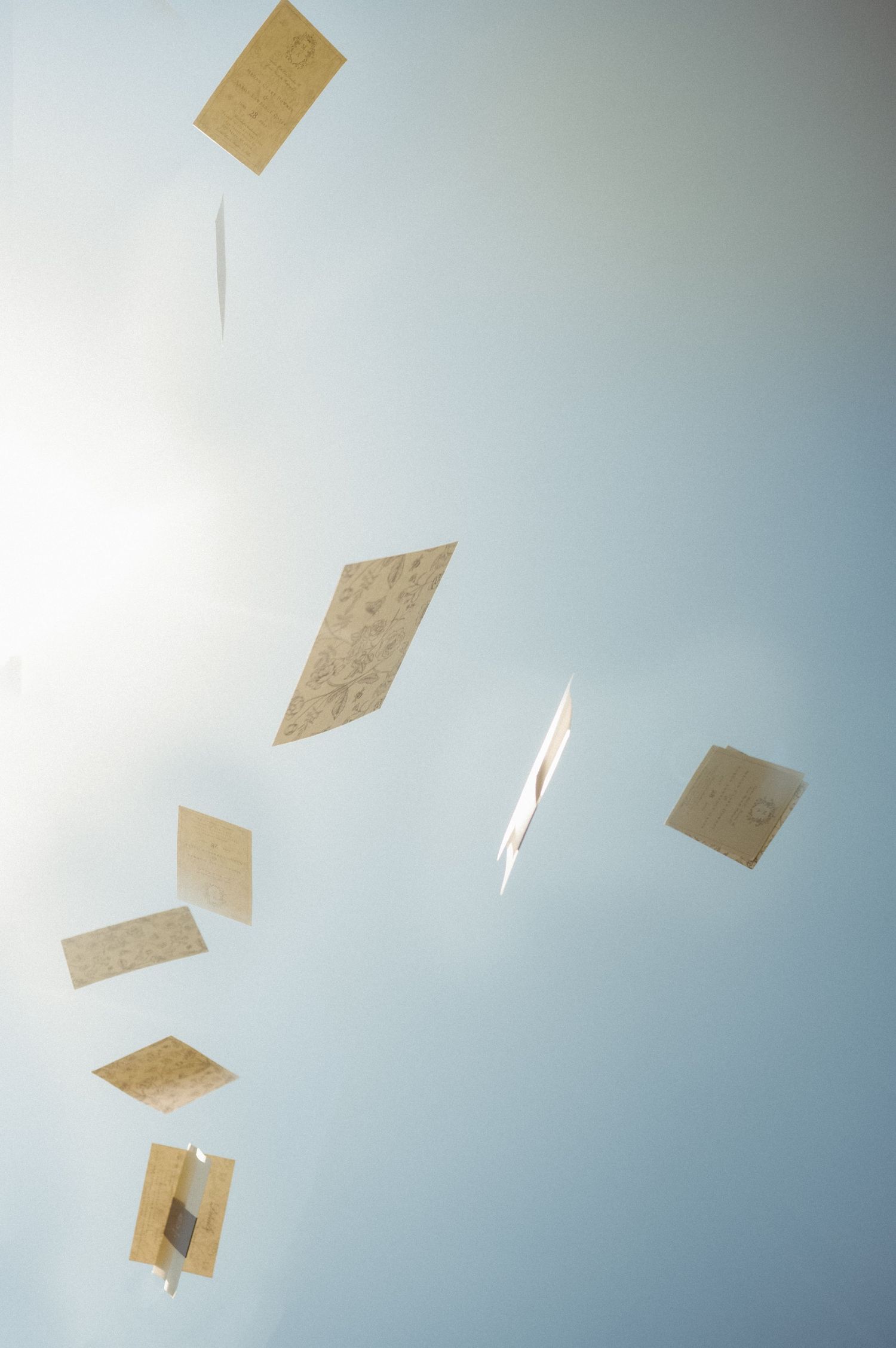 Paper airplanes float against a light blue sky in an artistic wedding detail shot.