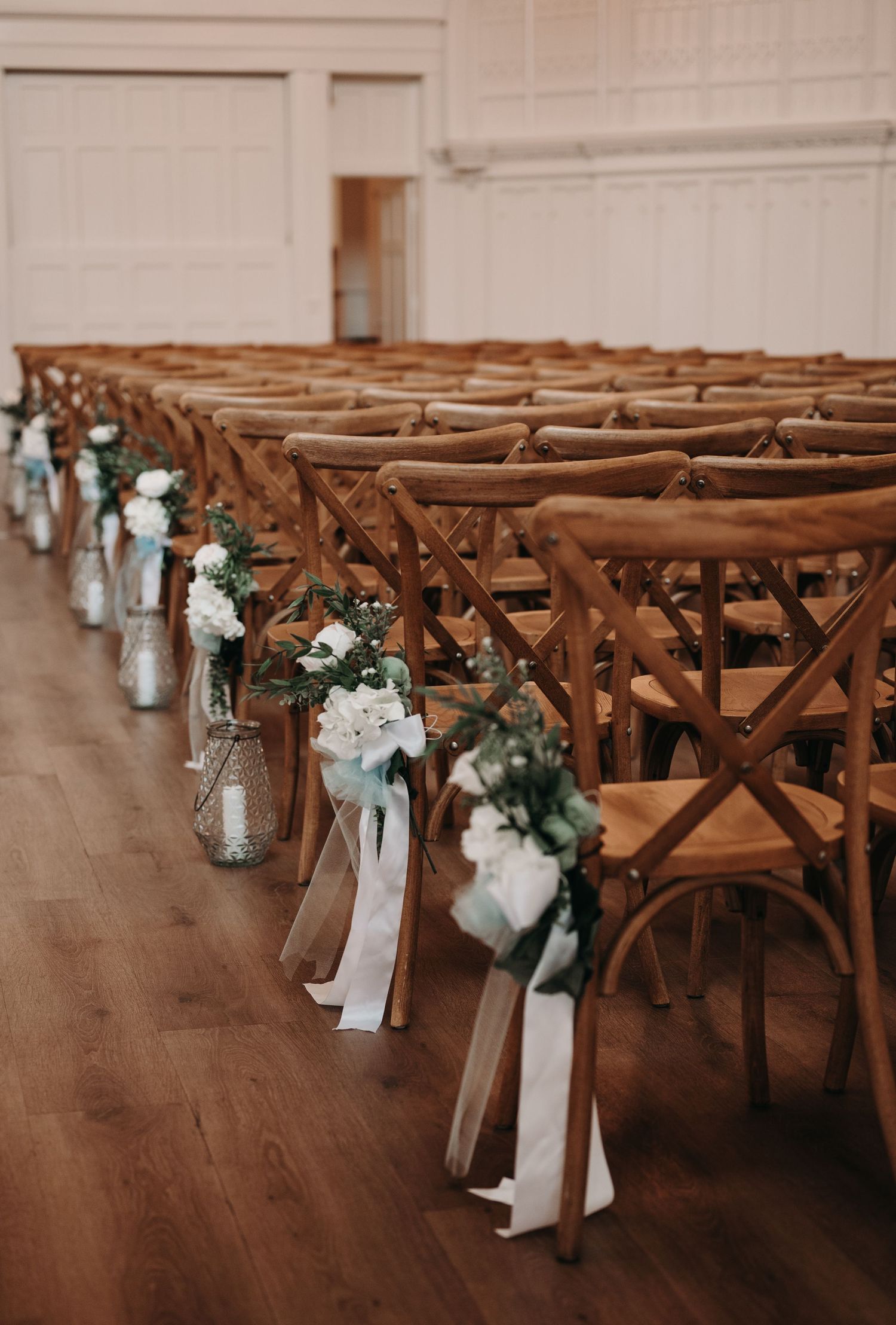 Rustic wooden chairs lined up for wedding ceremony with floral mason jar aisle decorations.