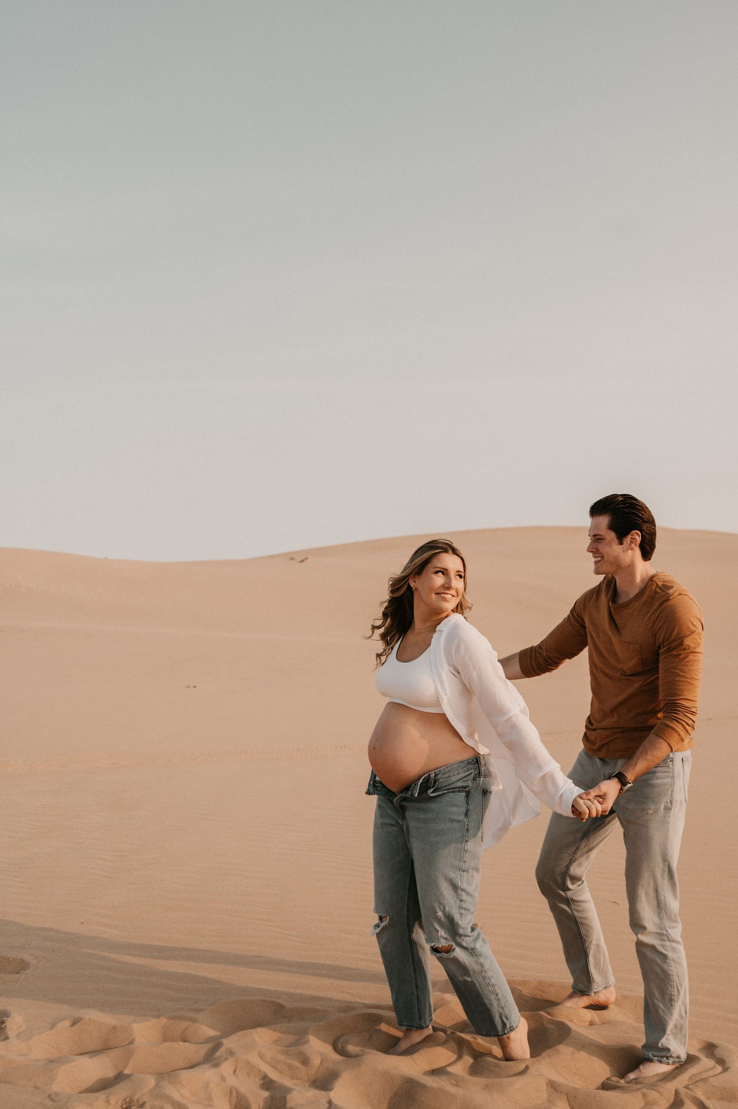 A couple enjoys a tender moment while standing on desert sand dunes.