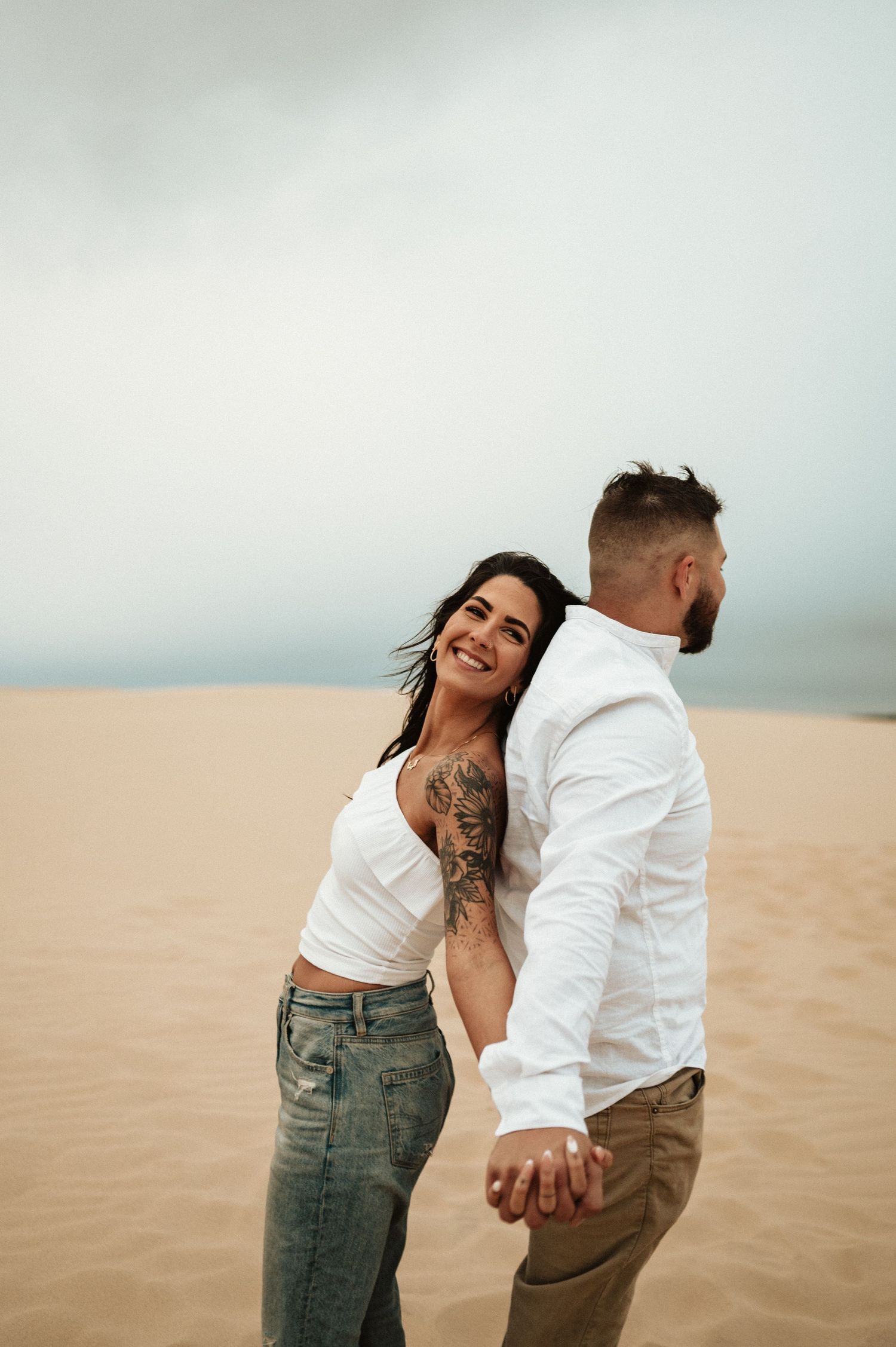A couple shares a joyful moment while holding hands on desert sand dunes.