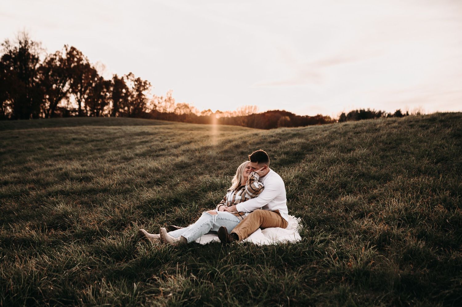 Couple sitting together on a blanket in a grassy field at sunset.