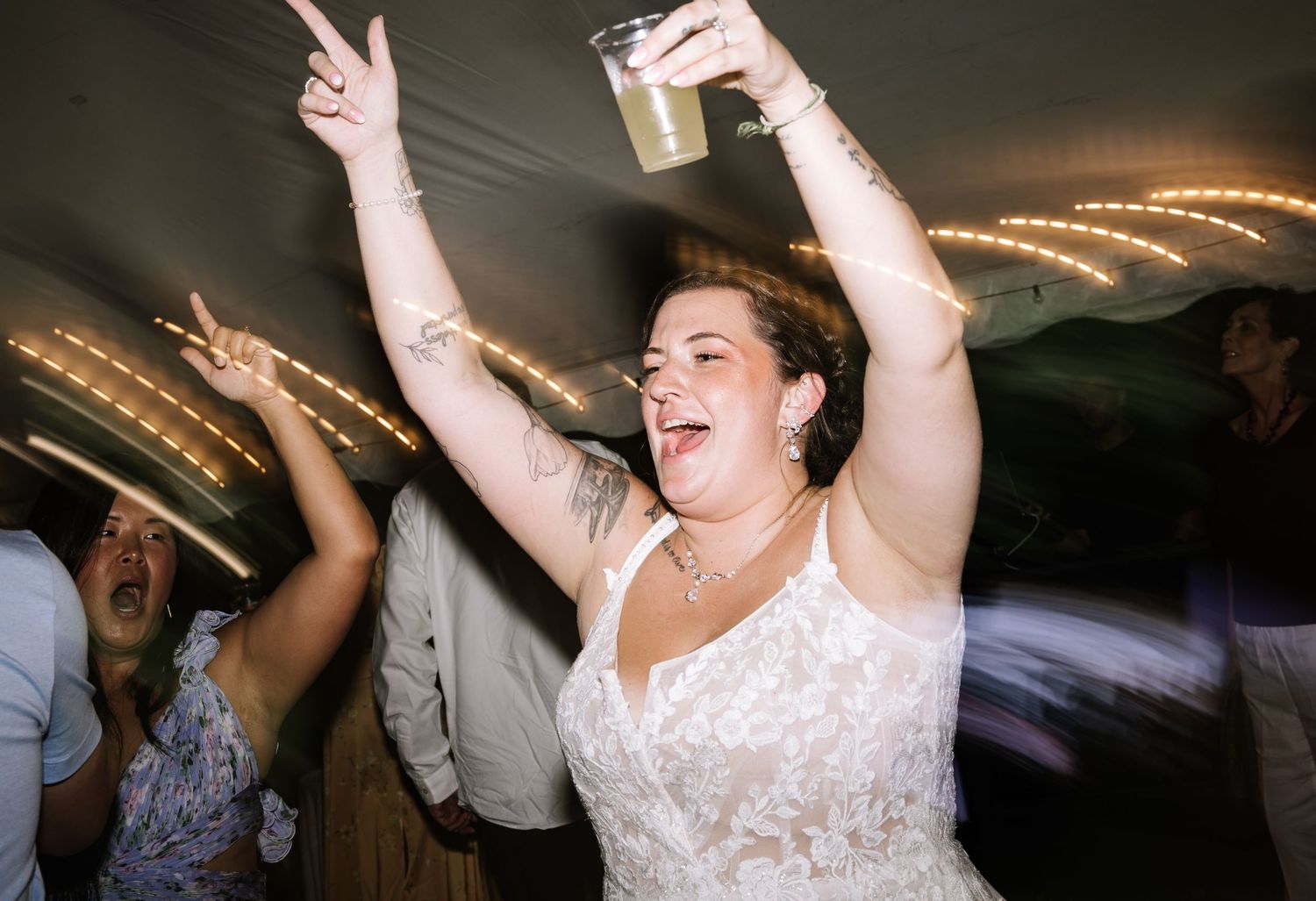 Energetic wedding reception dance party scene with guests celebrating under indoor lighting.