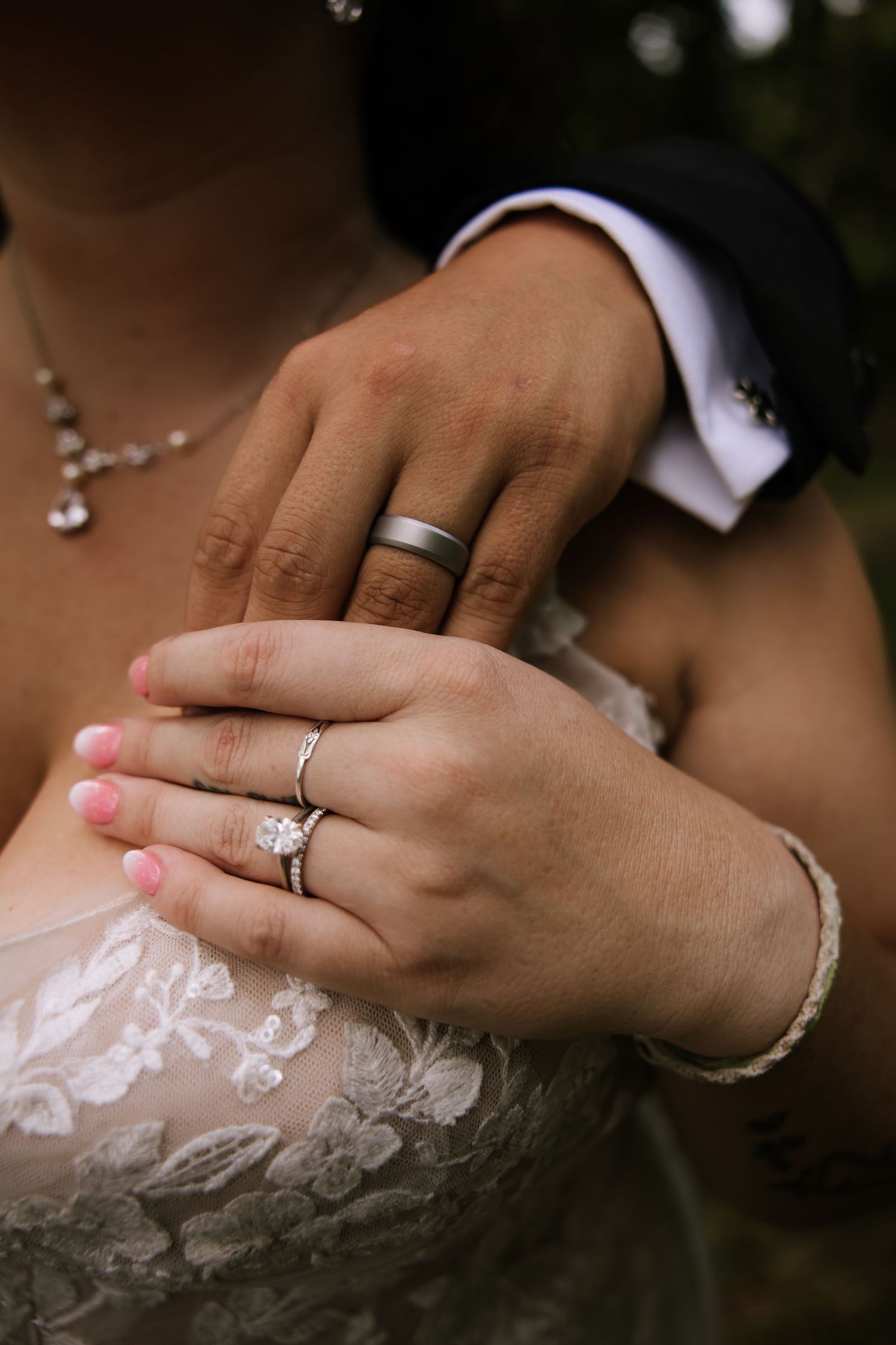 Close-up view of wedding rings and hands against delicate white lace fabric in romantic lighting.