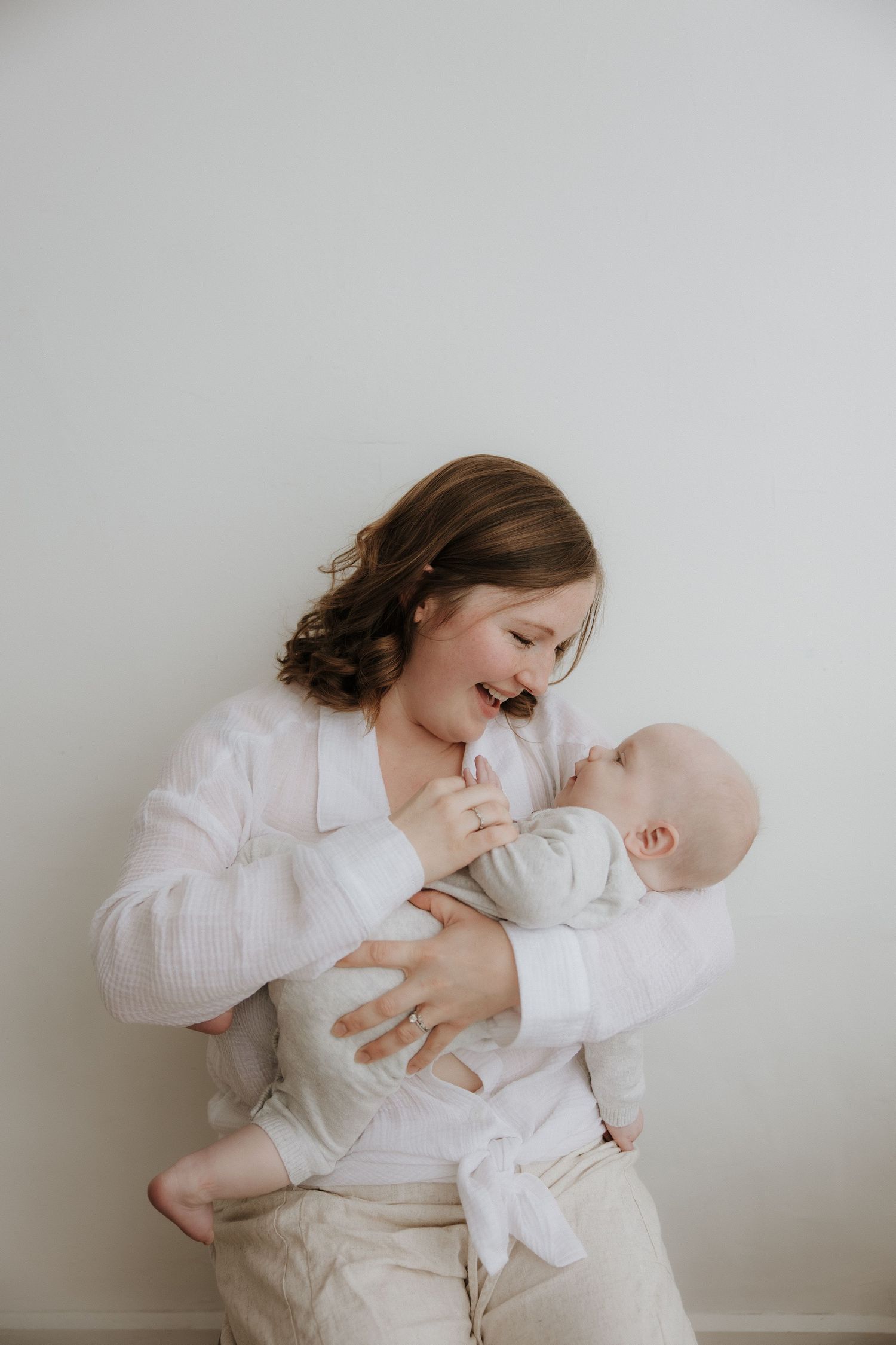 Smiling young girl in white top holding and bonding with newborn baby.