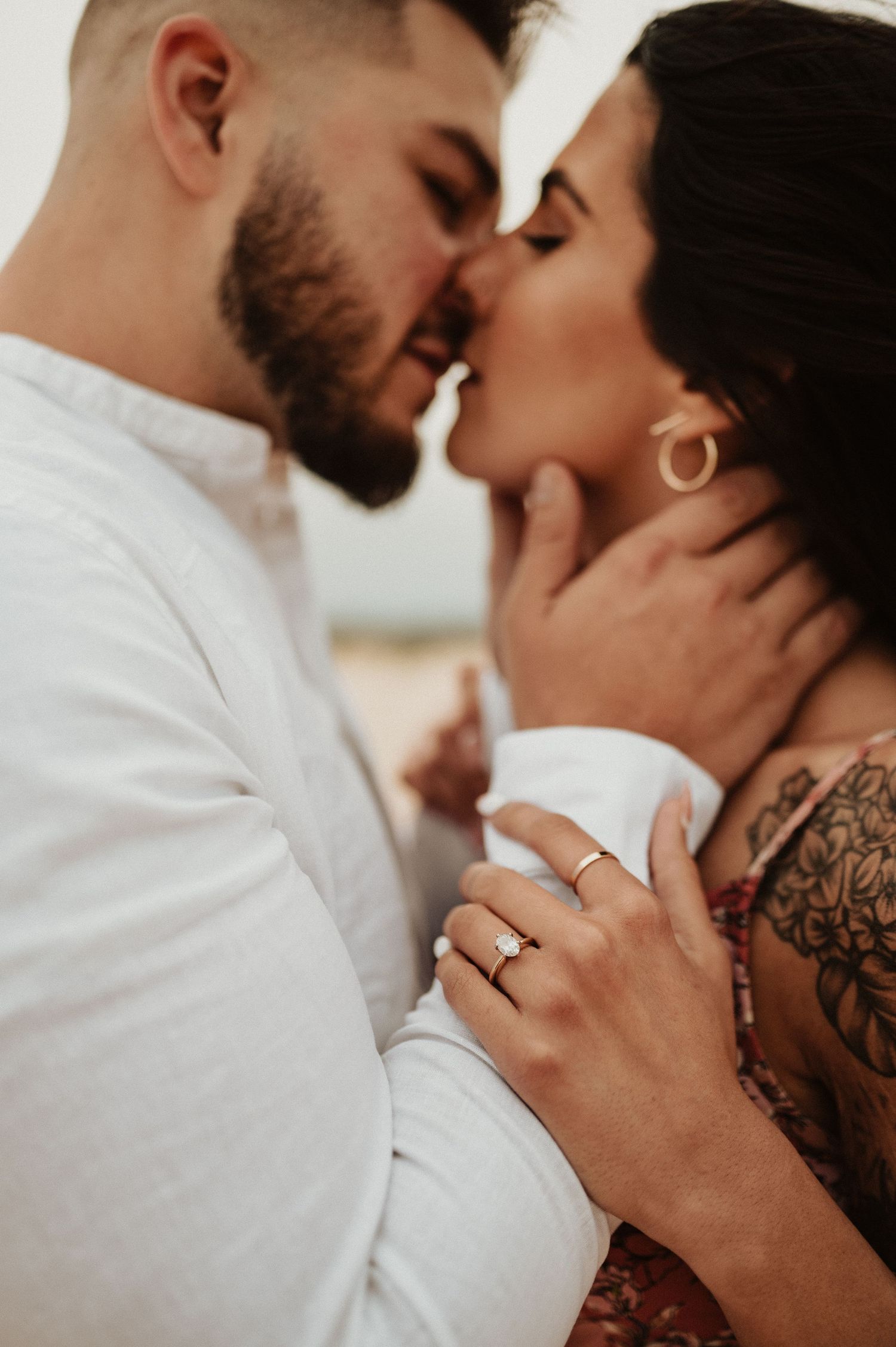 Close-up desert engagement photo showing tender intimacy between a couple with visible jewelry and tattoos.