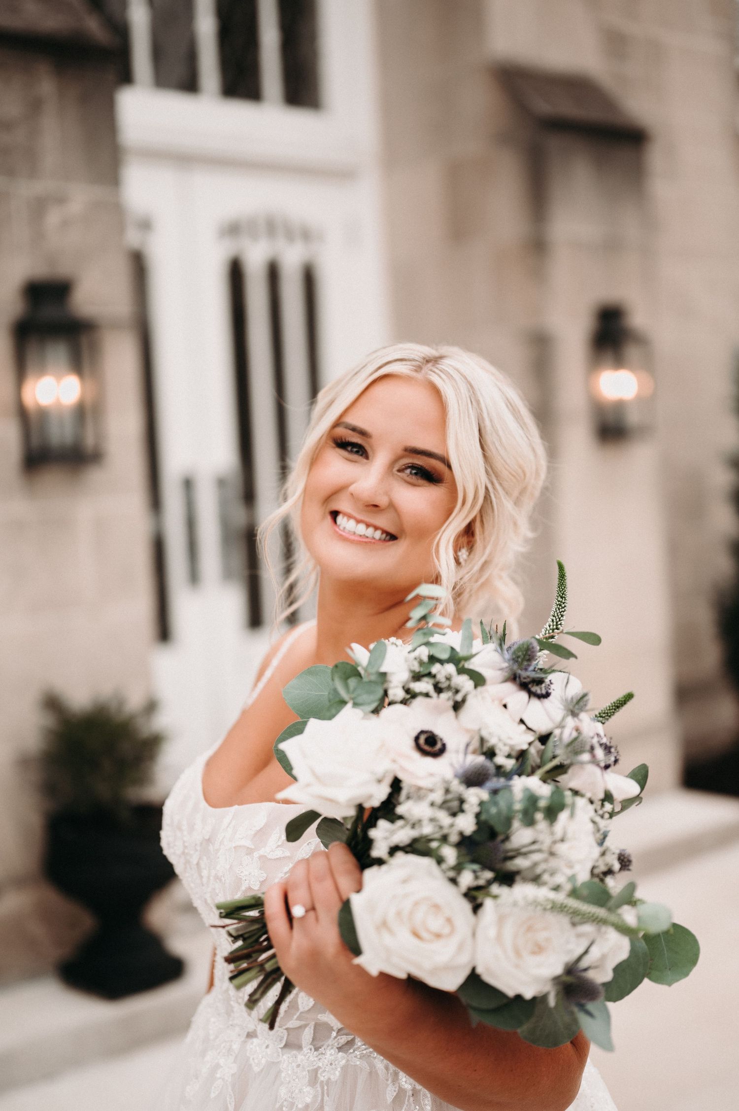 Close-up portrait of bride holding white and green wedding bouquet with joyful expression.