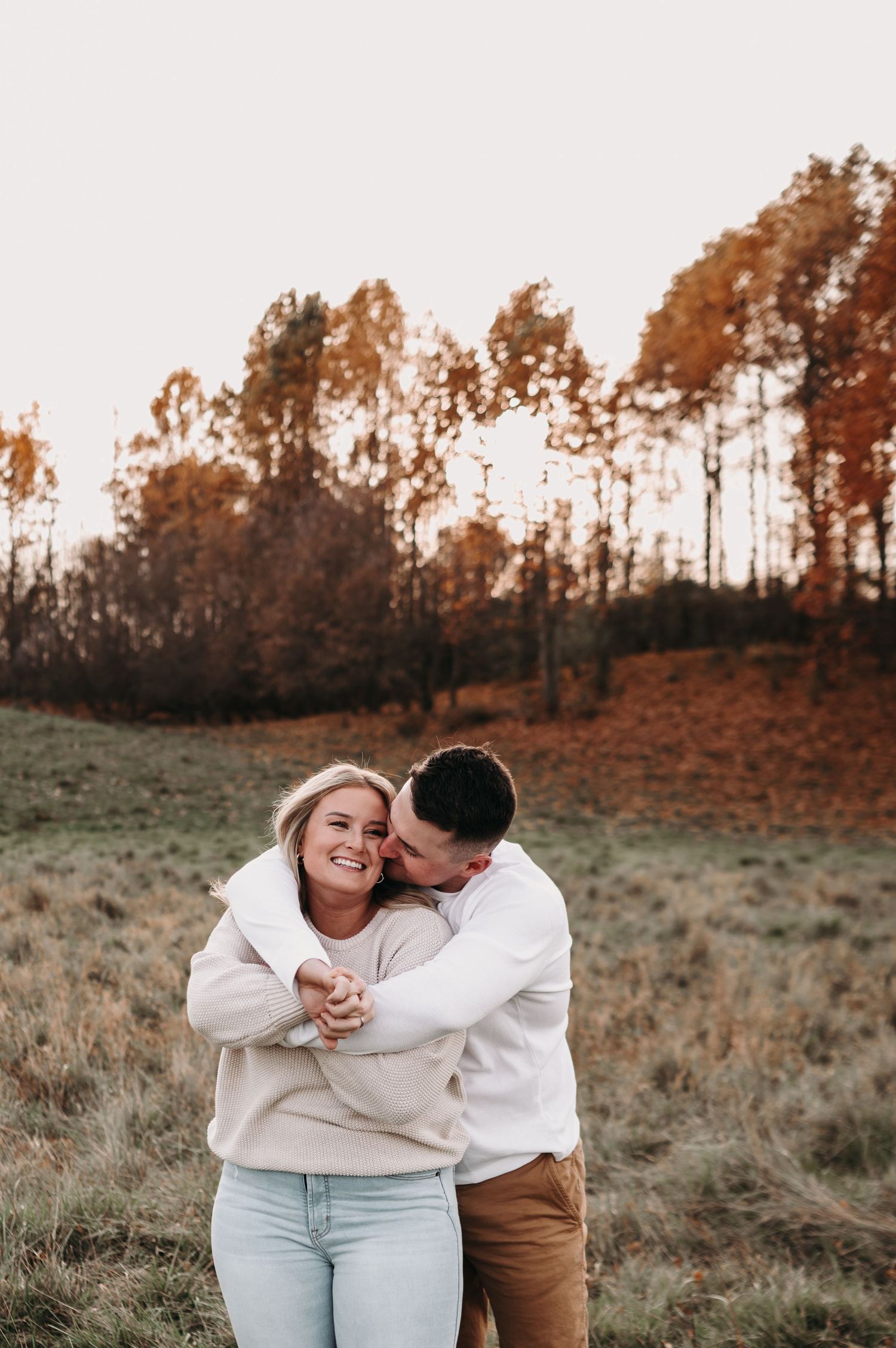 Romantic couple embracing and laughing together in autumn field with golden trees.