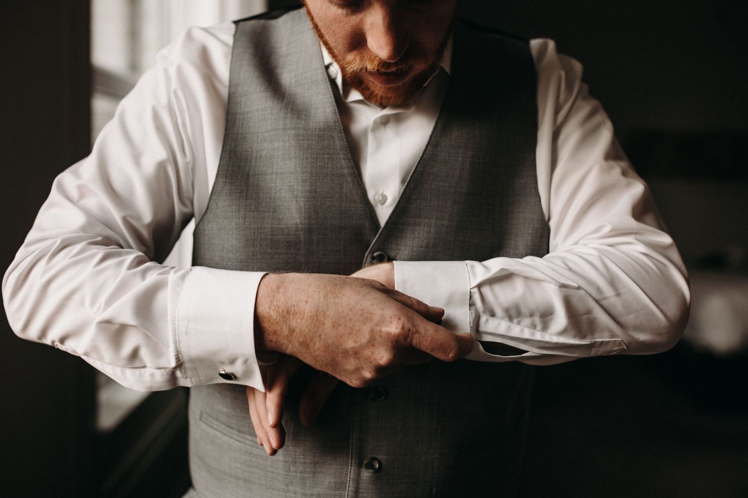 Close-up shot of someone adjusting the sleeve of their formal white shirt and grey vest.