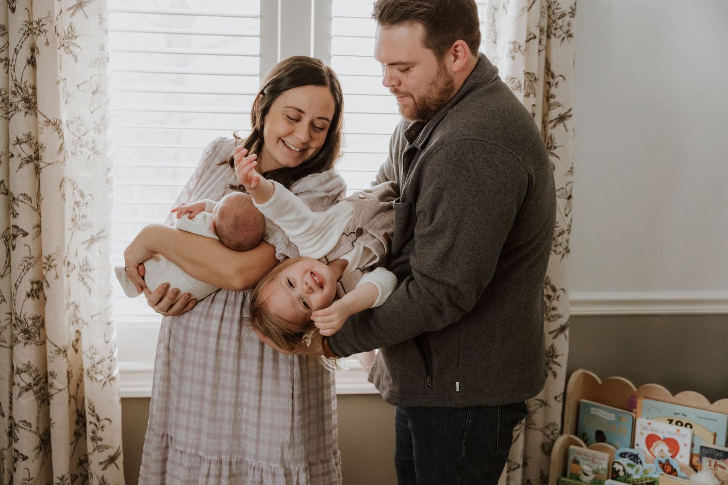 Parents sharing a tender moment with their newborn baby in a sunlit nursery.