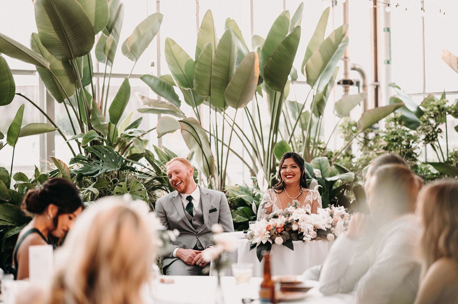 Wedding celebration in a greenhouse with guests enjoying the reception among tropical plants.