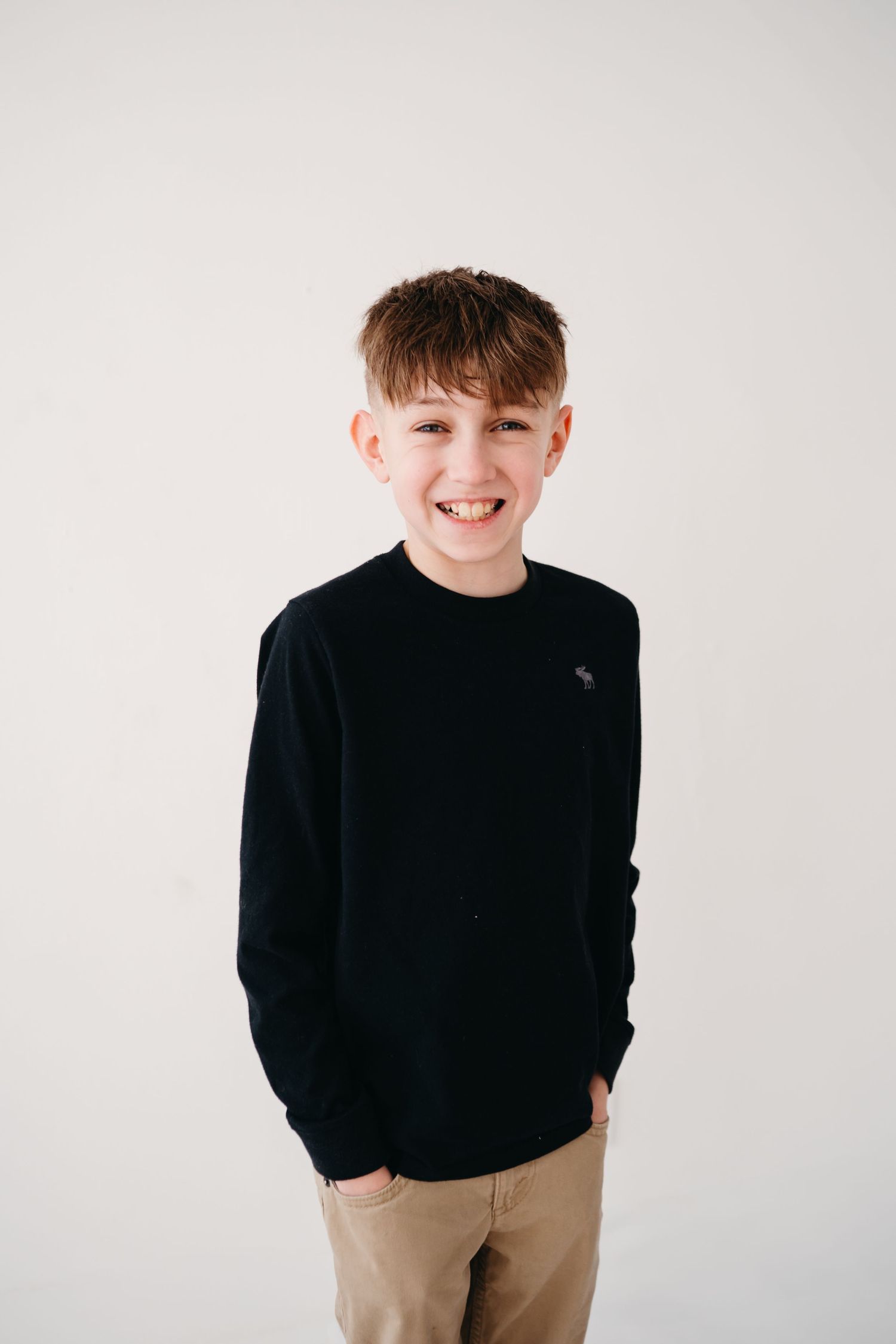 Young person wearing a black sweater and khaki pants smiles at camera against white background.