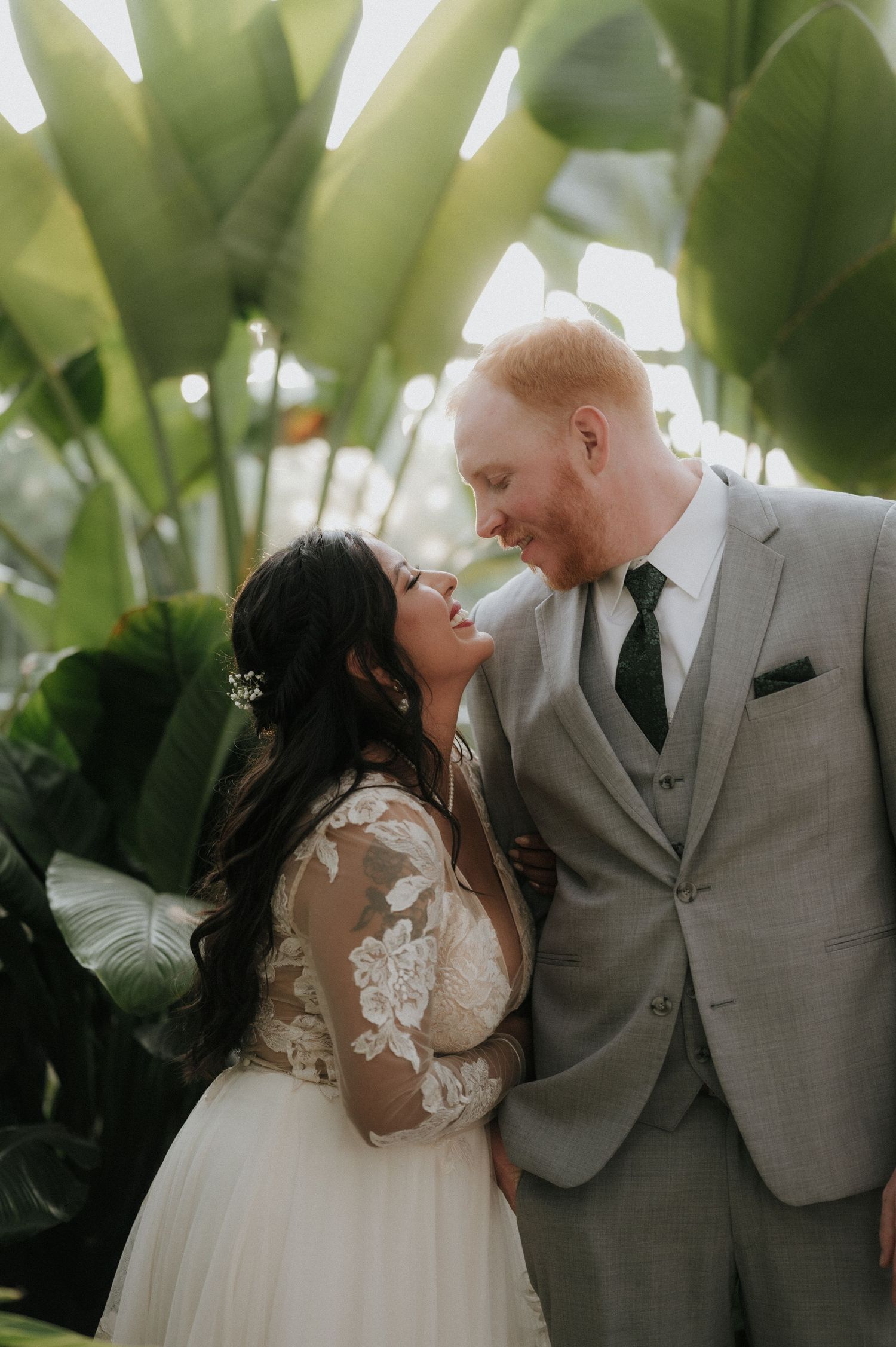 Romantic wedding couple poses among tropical plants and greenery in an intimate garden setting.