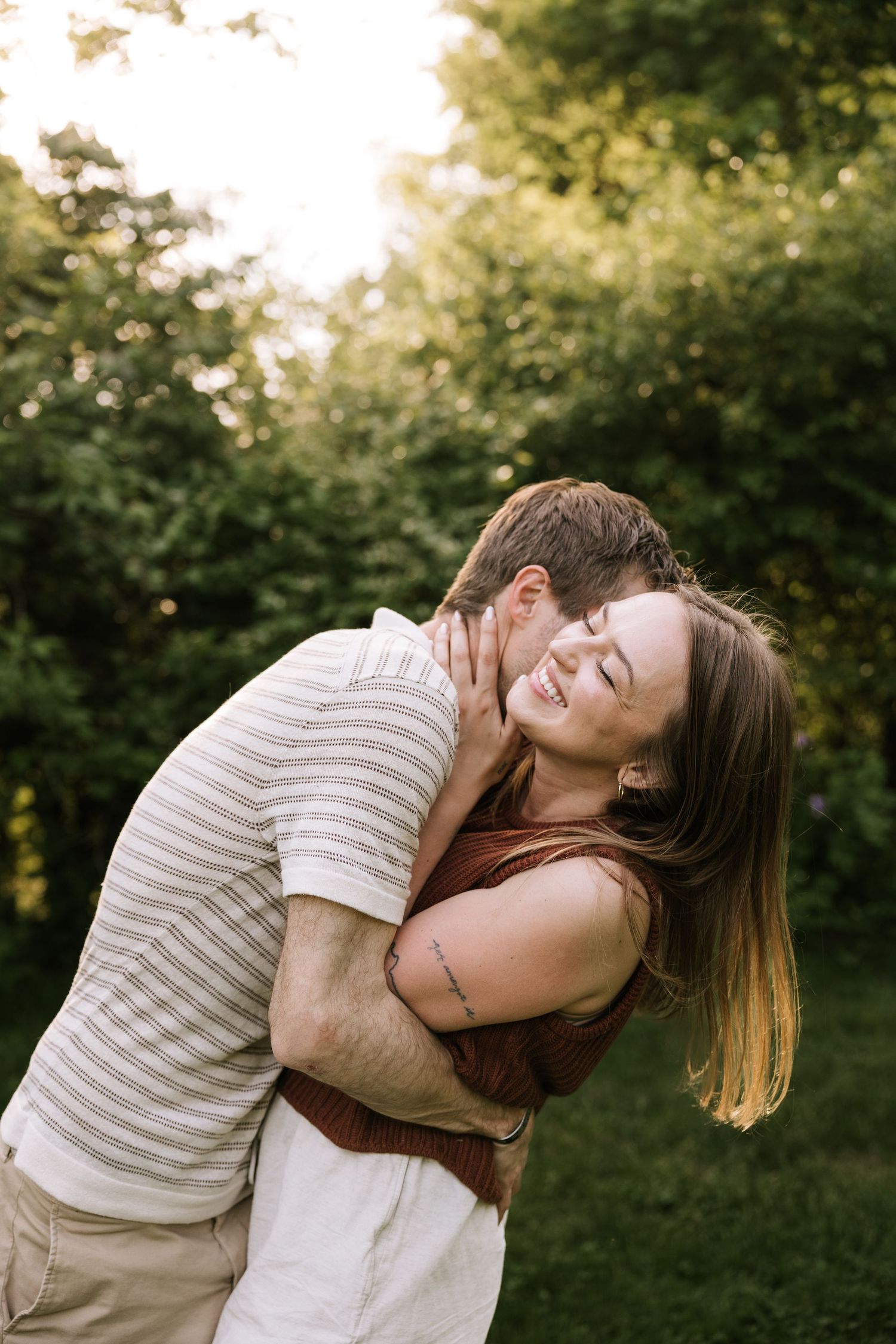 A happy couple shares a tender embrace outdoors, with the man kissing the smiling woman's cheek.