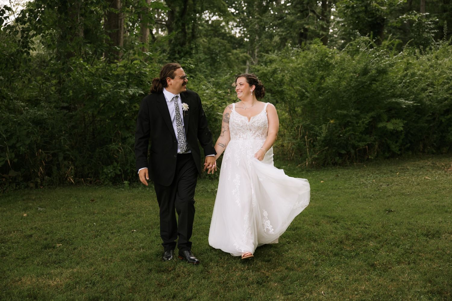 Newlyweds strolling hand in hand through a lush green outdoor setting.