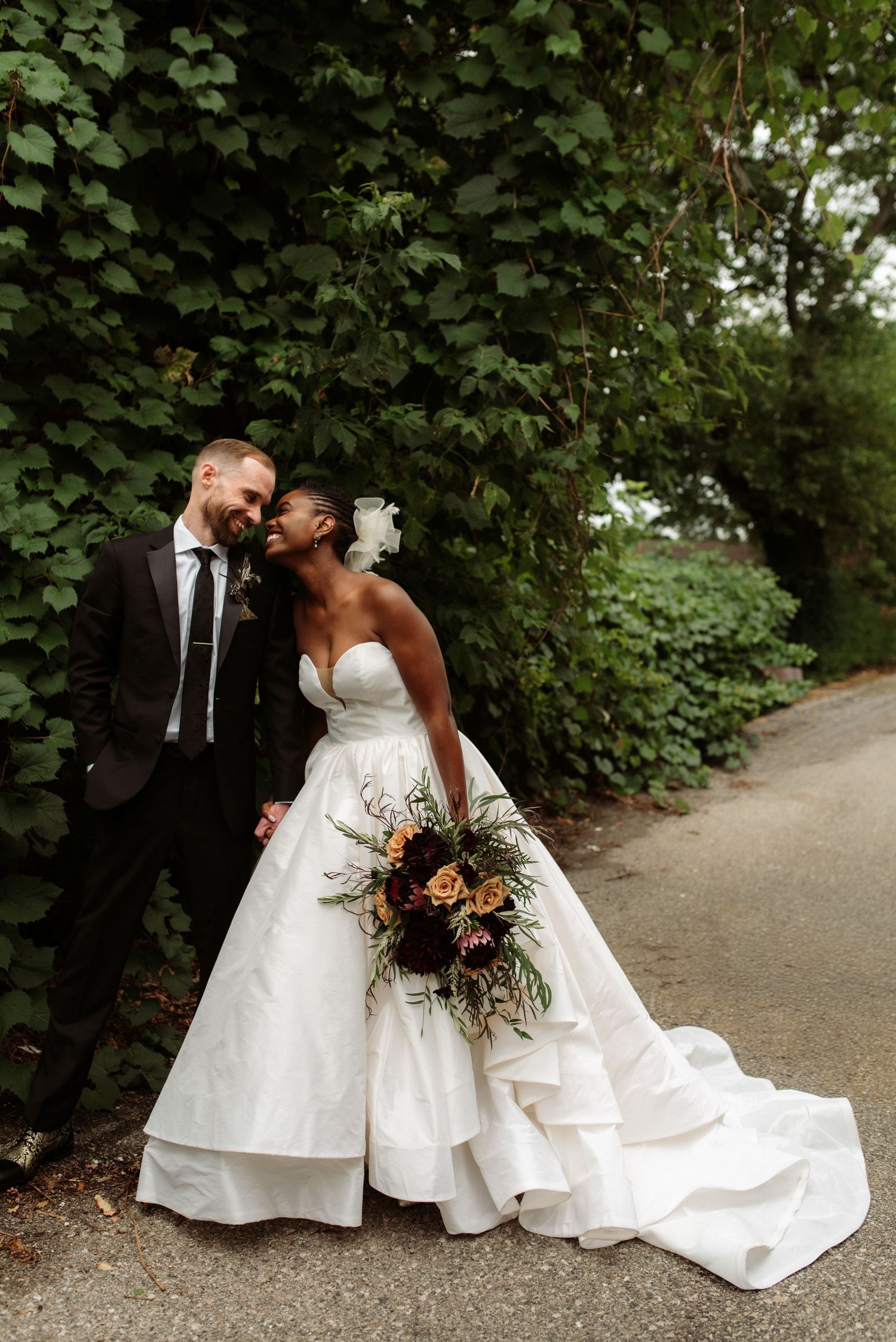 Wedding couple shares tender moments on a tree-lined path in elegant white and formal attire.