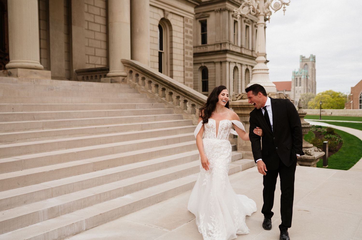 Bride and groom pose together on elegant stone steps of classical architecture.