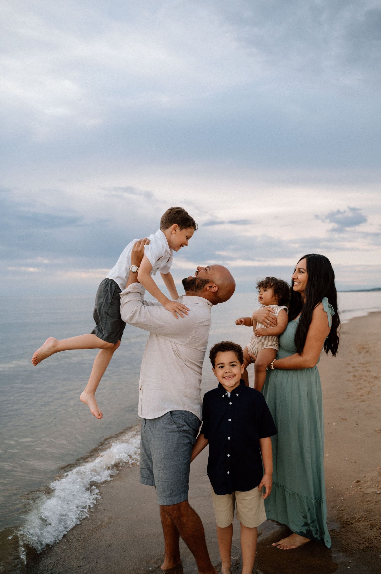 Family playing and embracing together on a beach at sunset.