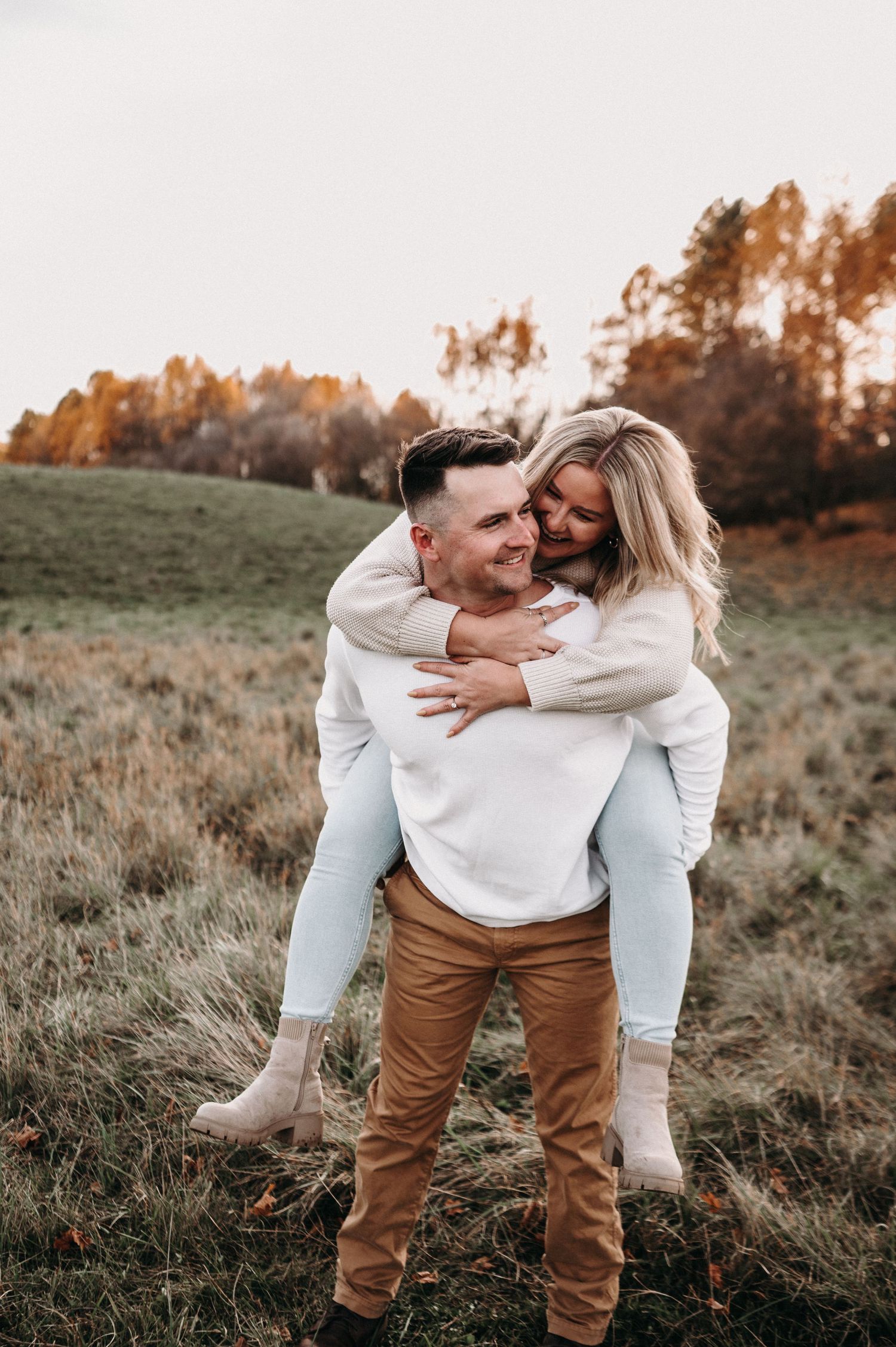 Playful piggyback ride in autumn field with warm sunset lighting and fall foliage.