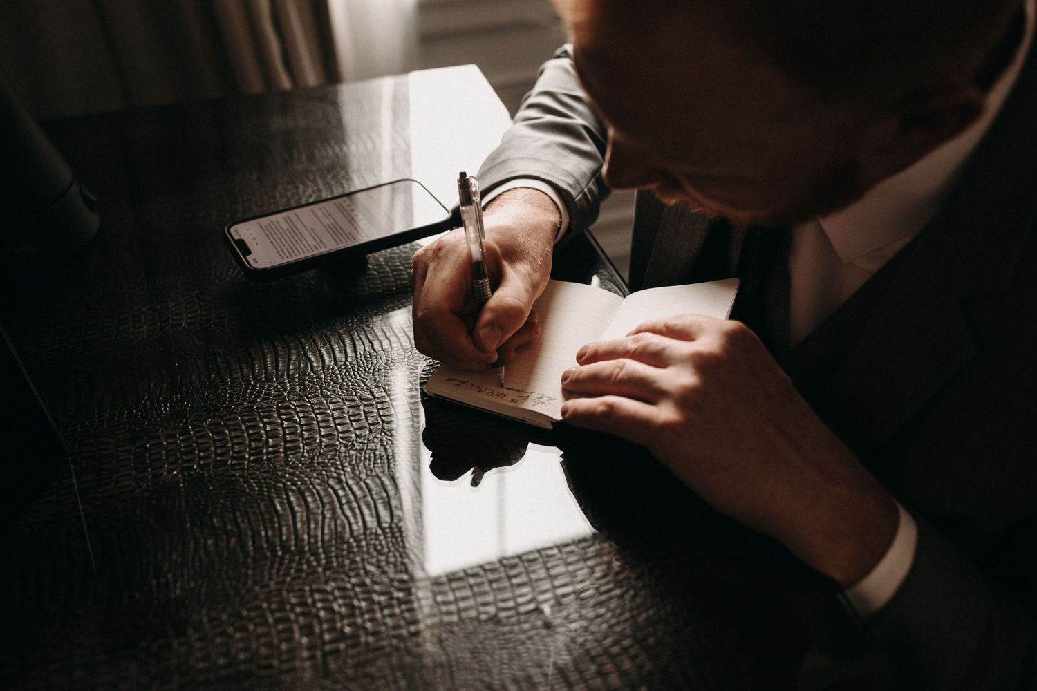 Overhead view of hands writing on paper at a dark wooden table.