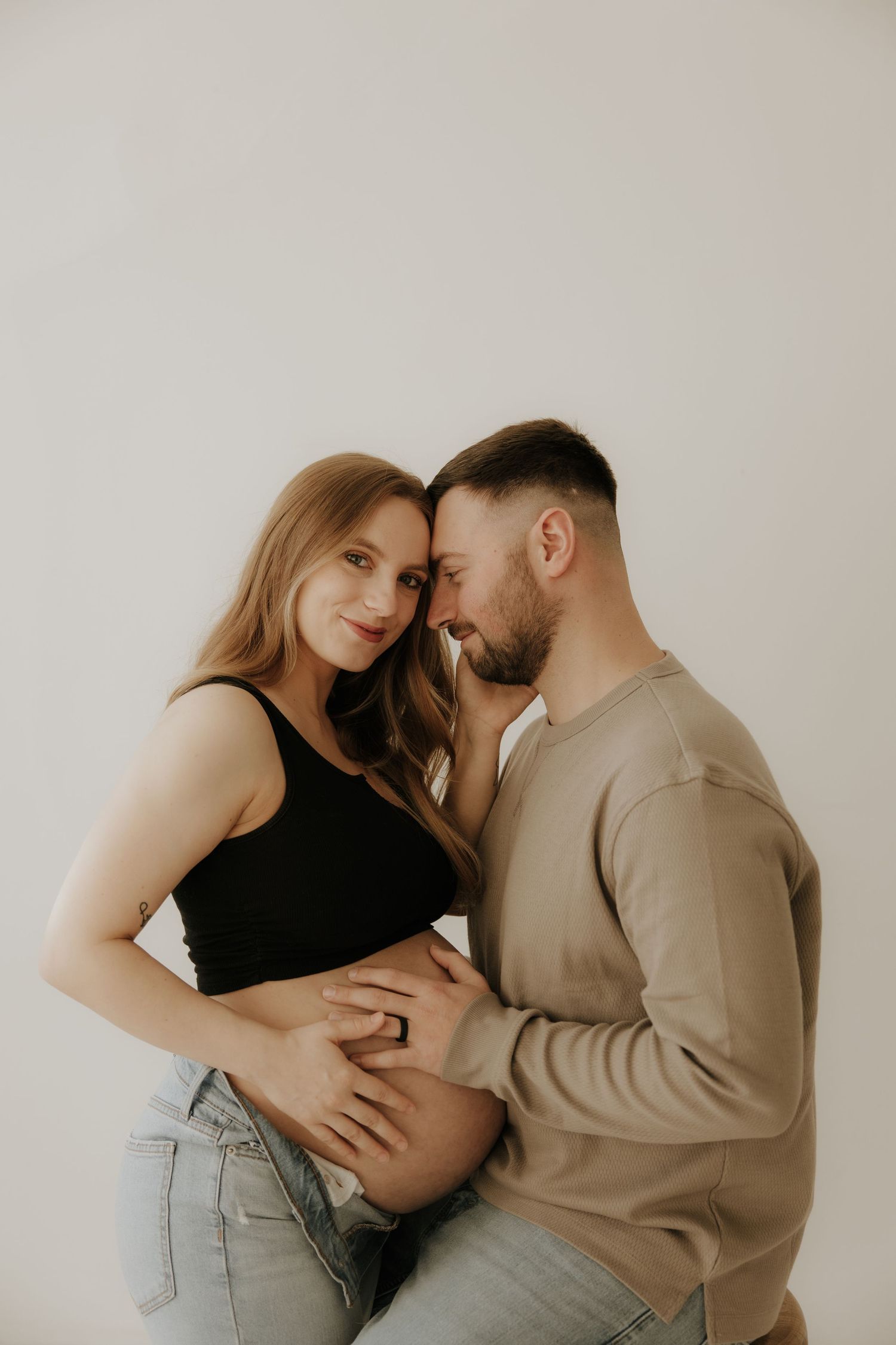 Romantic maternity portrait showing gentle embrace against minimalist white backdrop.