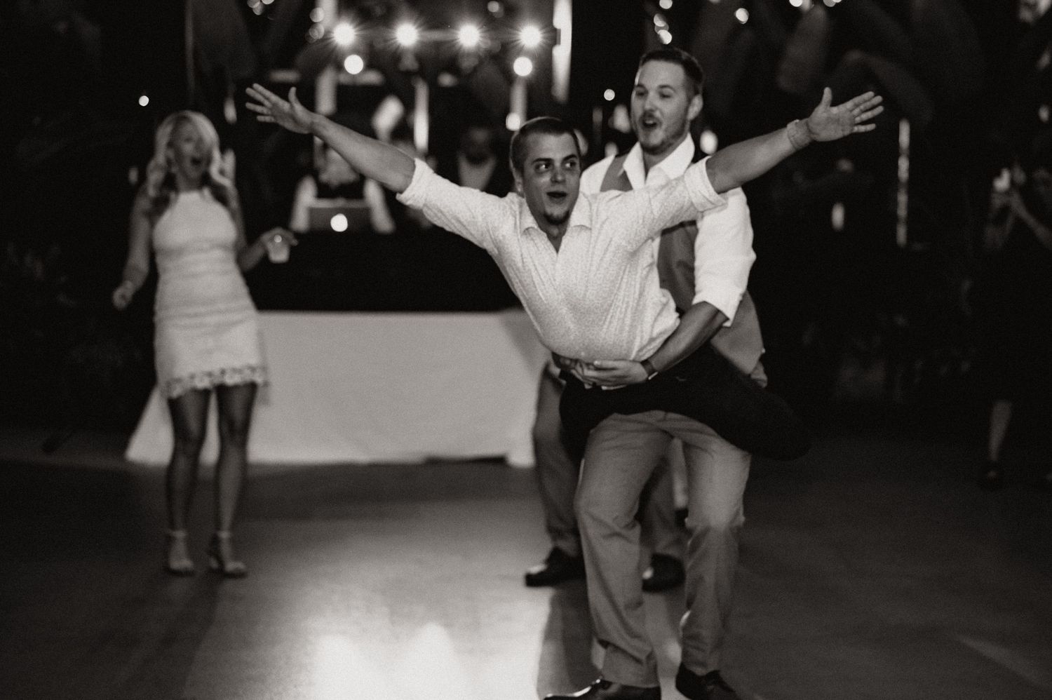 Wedding guests dancing with arms outstretched during reception celebration.