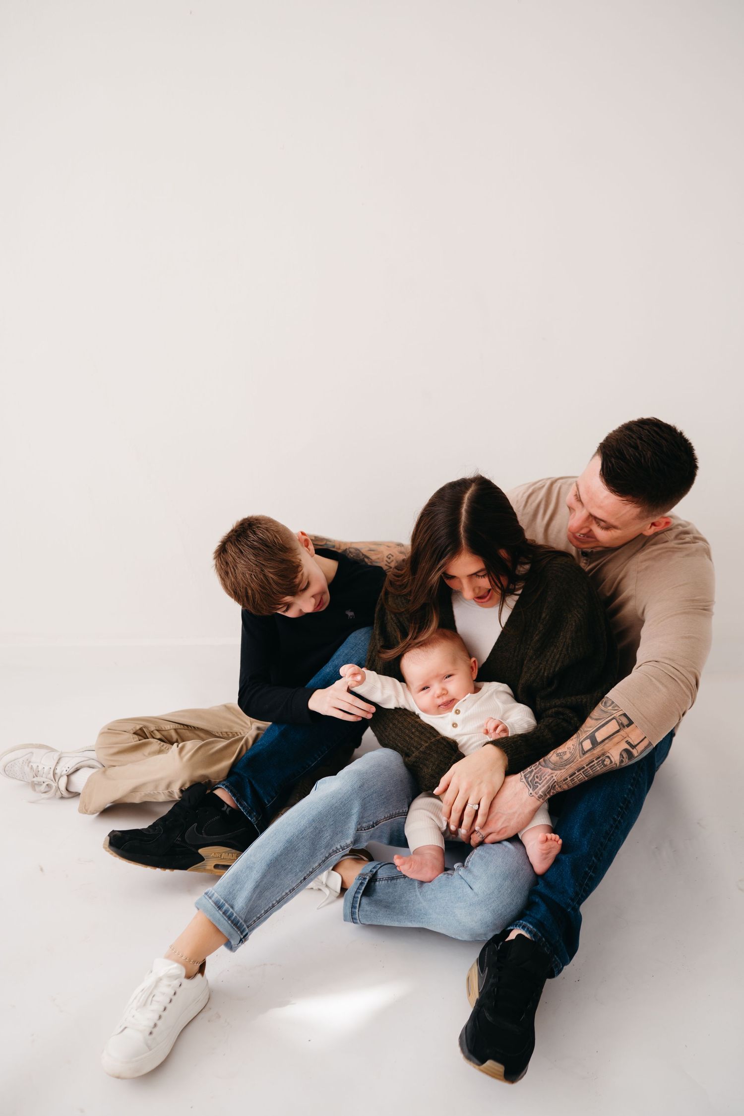 Family cuddles together on white floor during intimate lifestyle photo session.