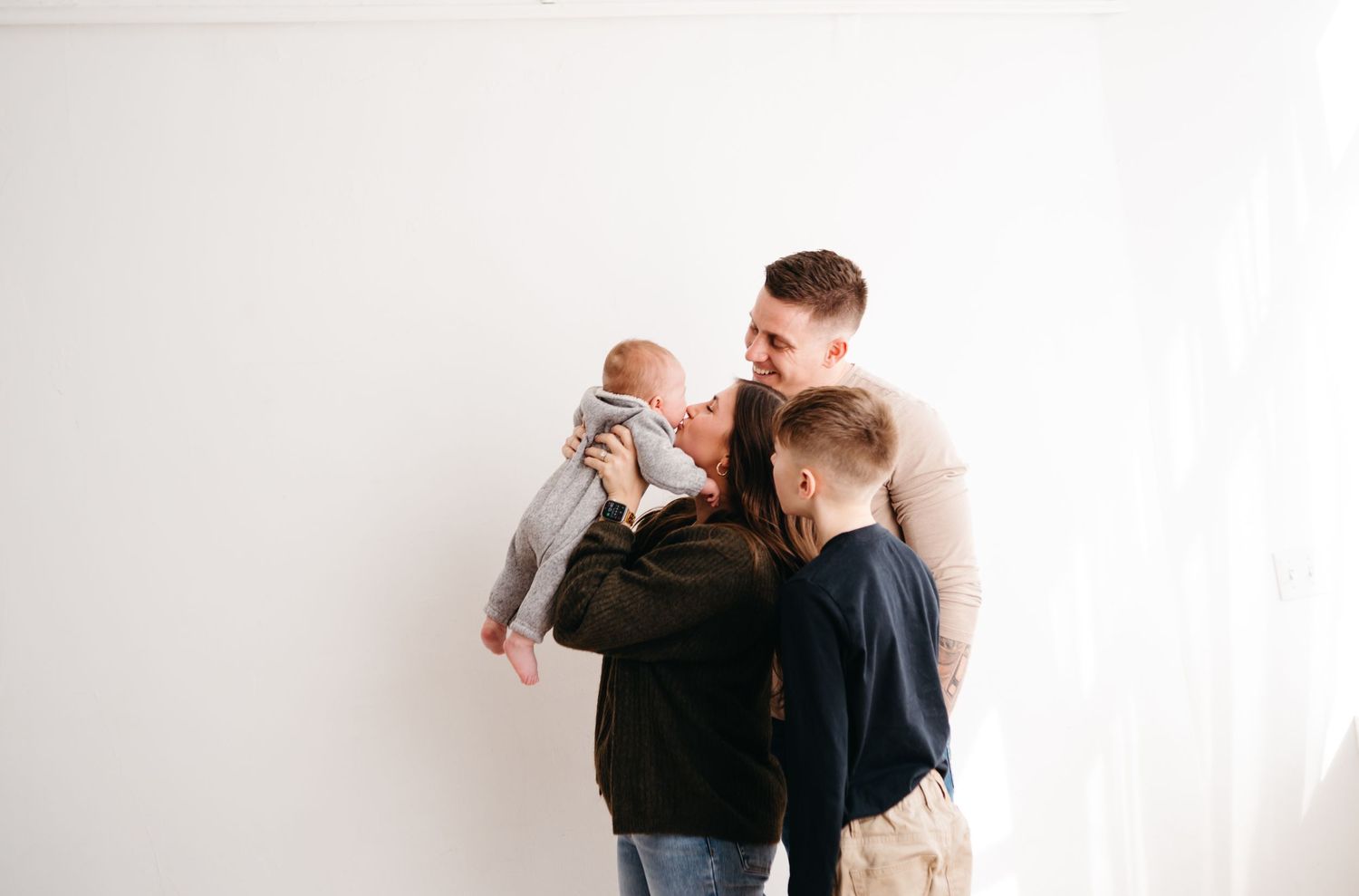 Family gathering with three people standing together against white wall.
