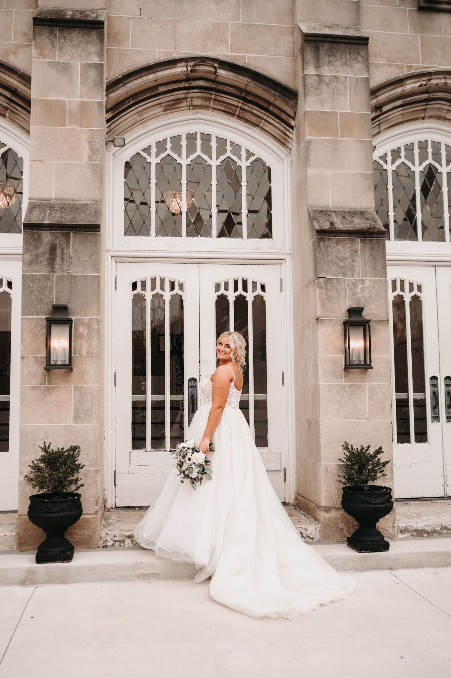 Bride in flowing white gown poses by Gothic church entrance with lanterns.