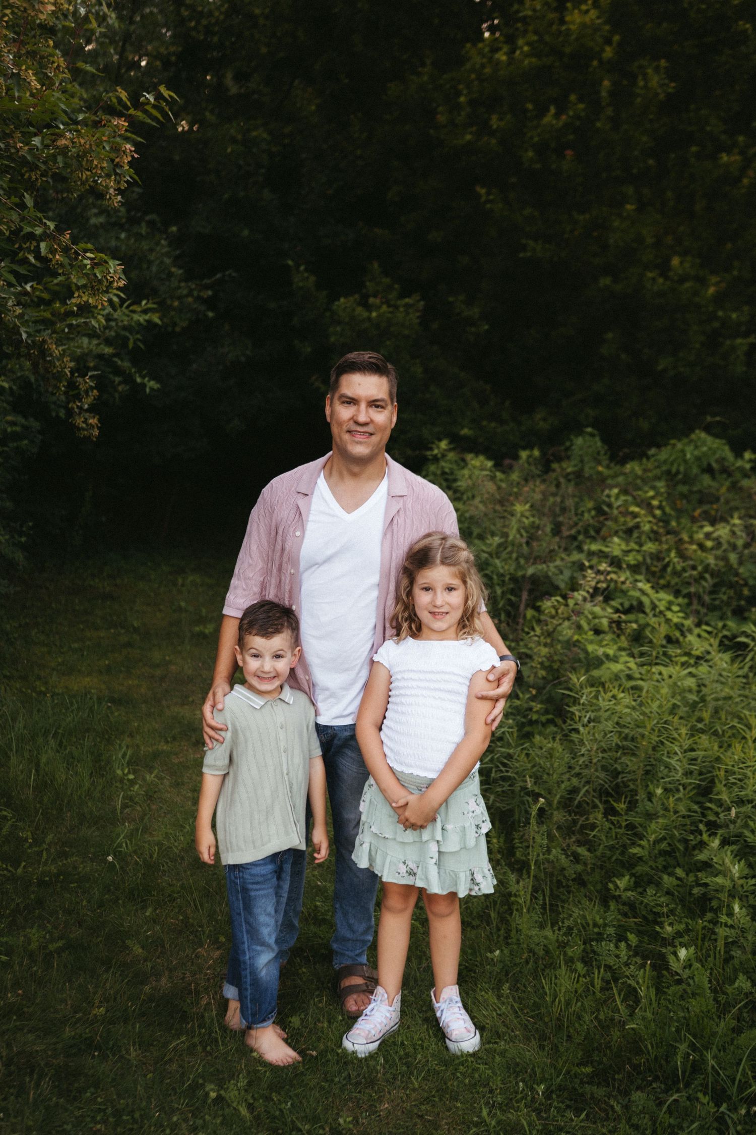 Young children pose together during outdoor family photo session in green natural setting.