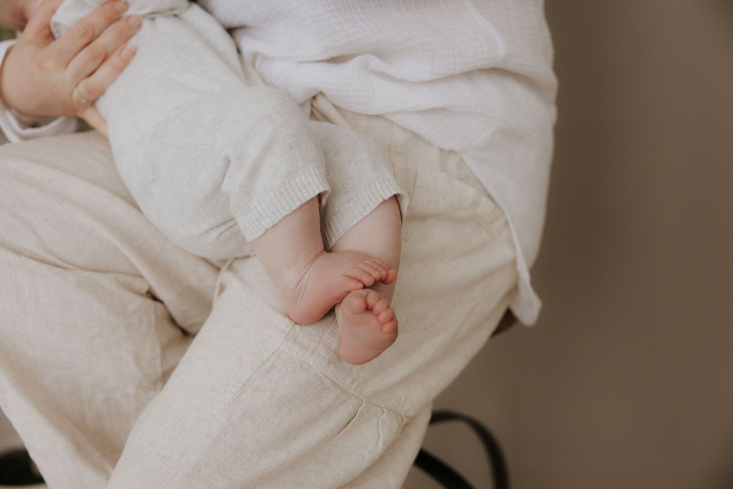 Newborn baby tiny feet peeking out from white linen pants while being held by a parent.