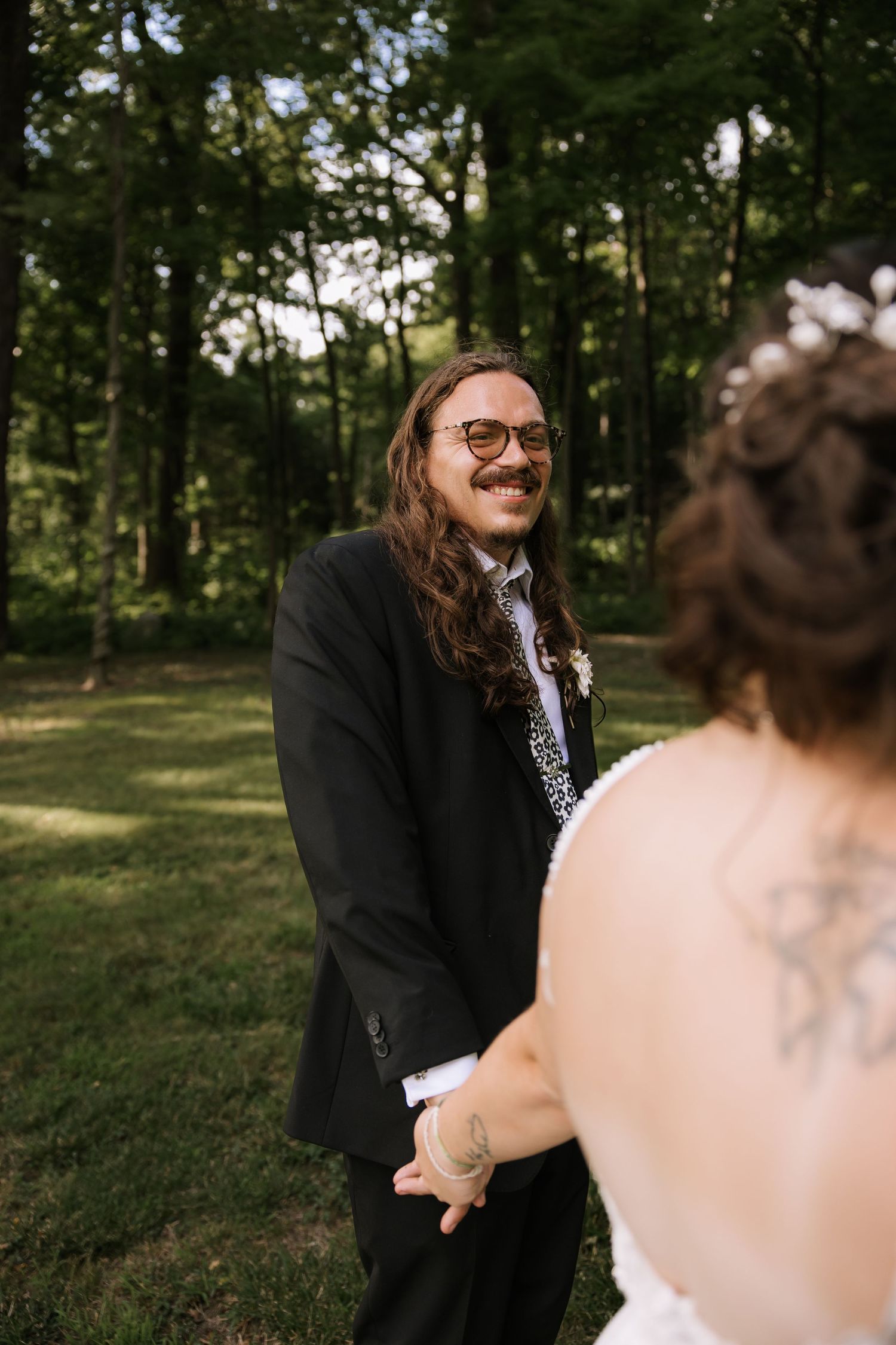 Couple shares a joyful first look moment in a wooded outdoor setting.