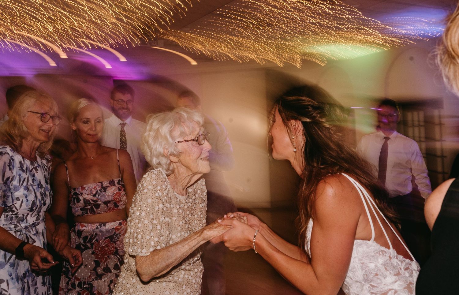 Wedding guests dancing and celebrating on a colorful illuminated dance floor at an evening reception.