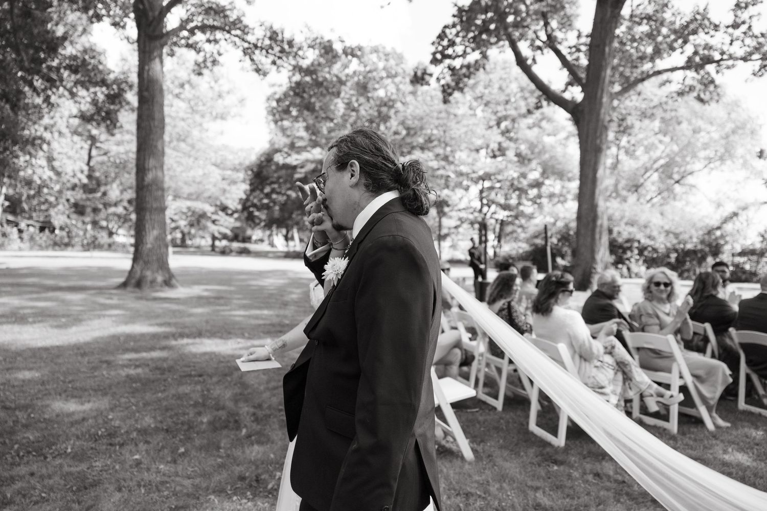 Black and white photo of wedding attendees seated in rows during an outdoor ceremony.