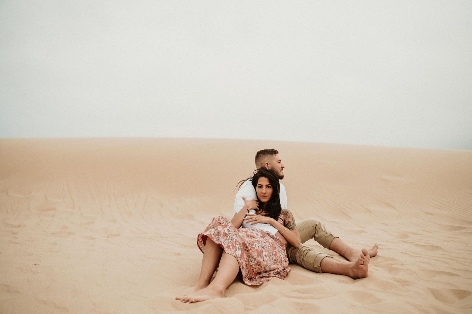 A couple relaxes together on desert sand during an intimate photoshoot.