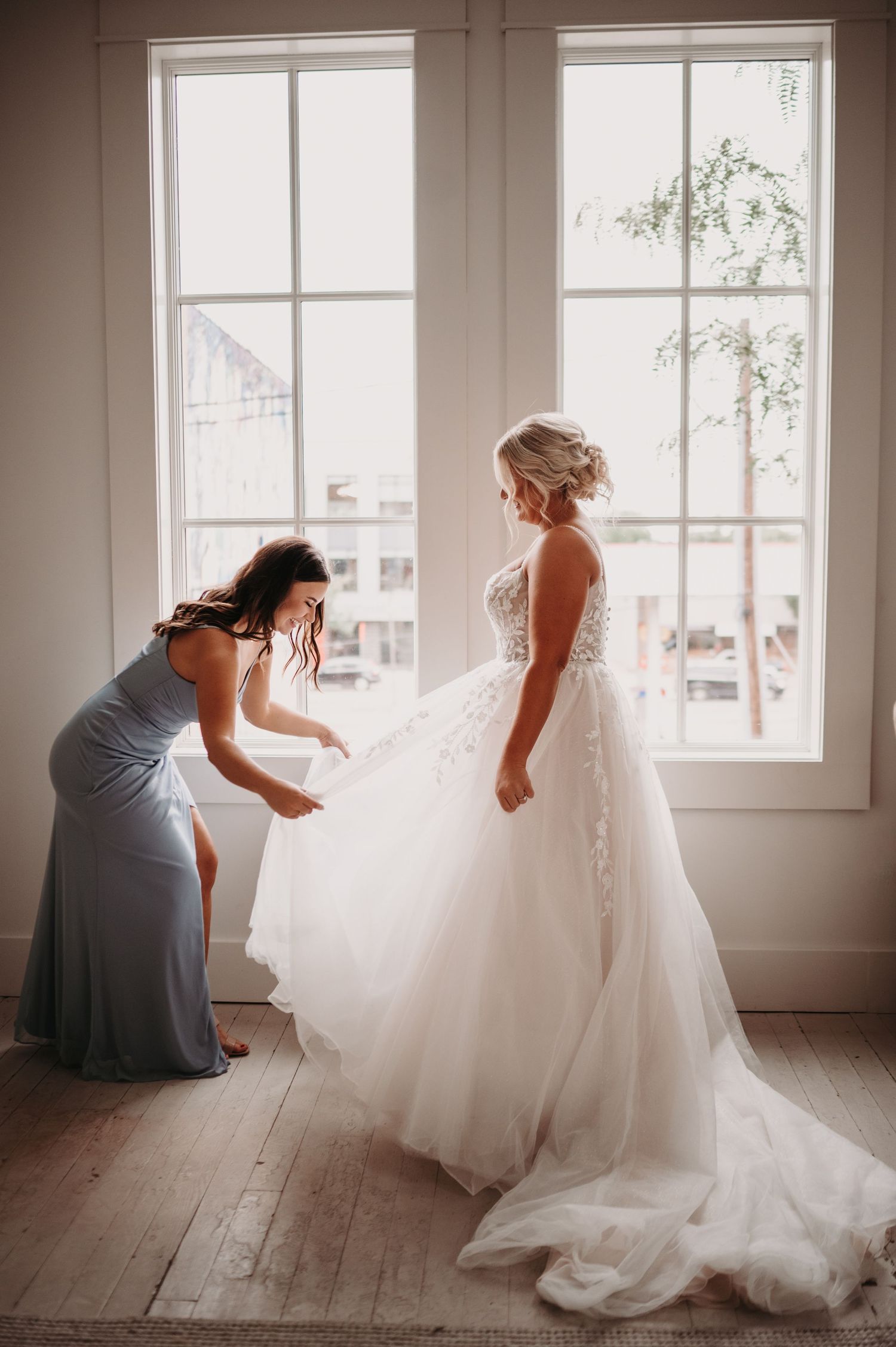 Final wedding dress adjustments being made in front of bright windows.