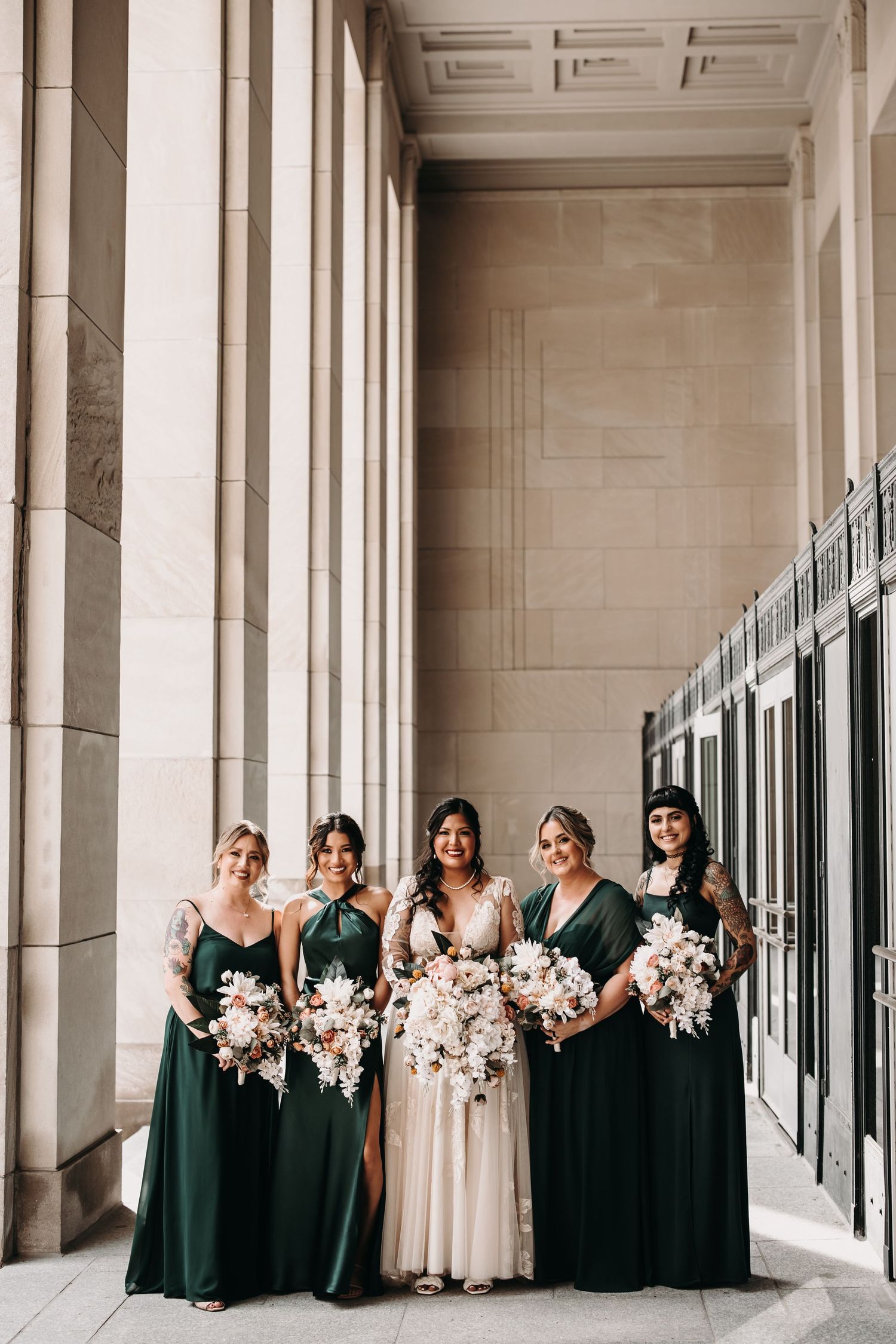 A wedding party poses in an elegant colonnade with stone pillars and classic architecture.
