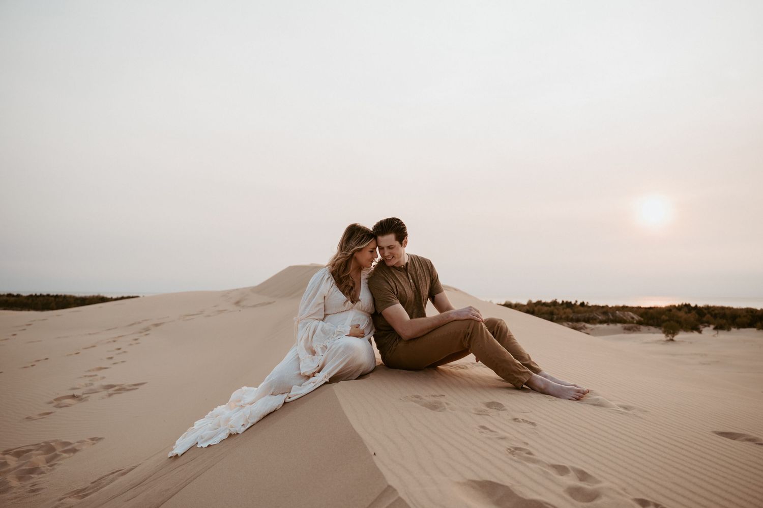 A couple embraces on golden sand dunes during a desert sunset.