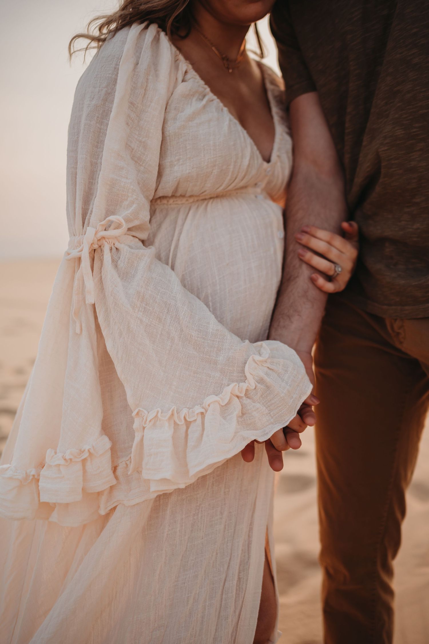Close-up detail of a flowing white dress and intimate embrace in desert lighting.